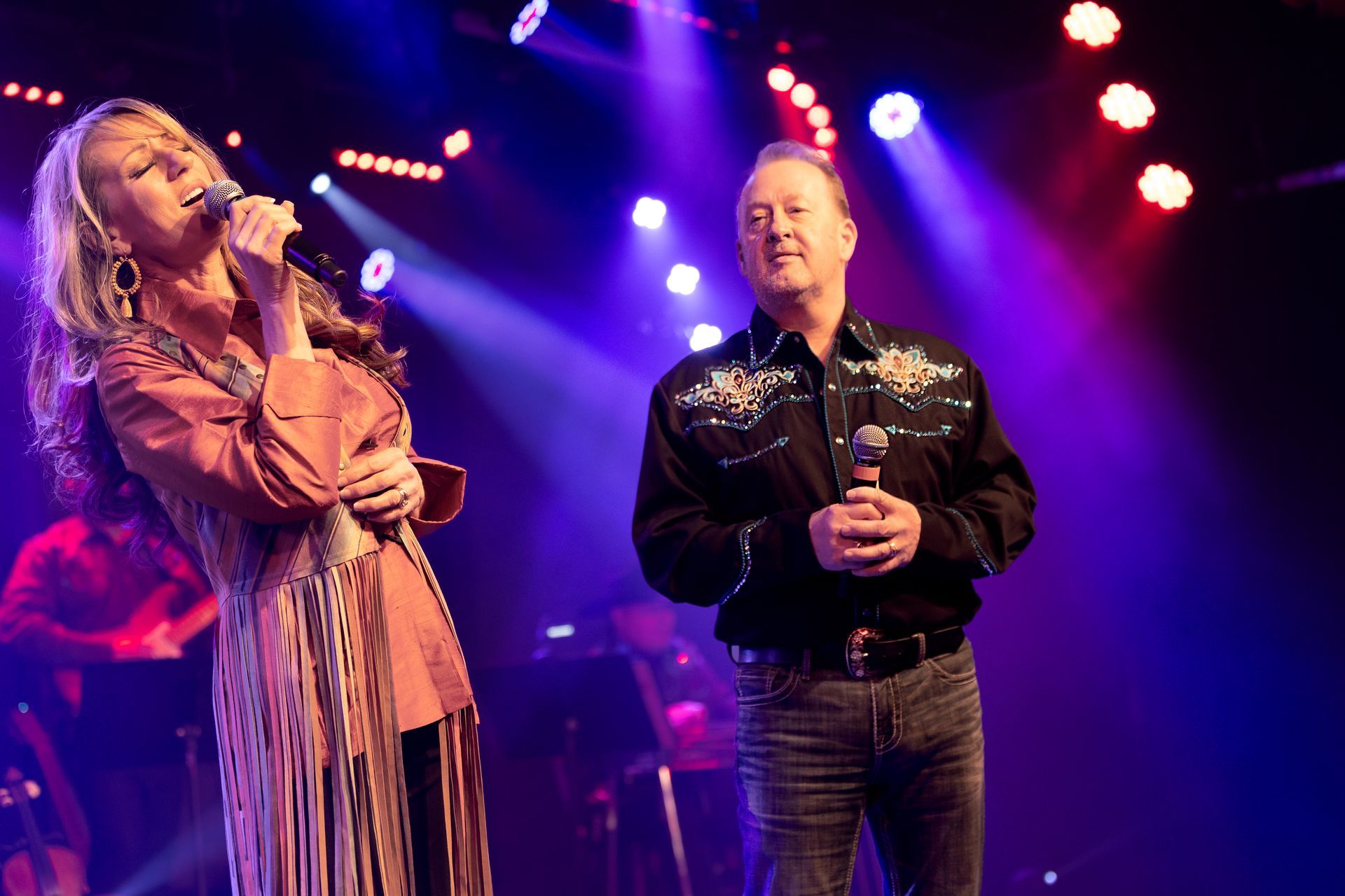 A man and a woman are singing into microphones on a stage.