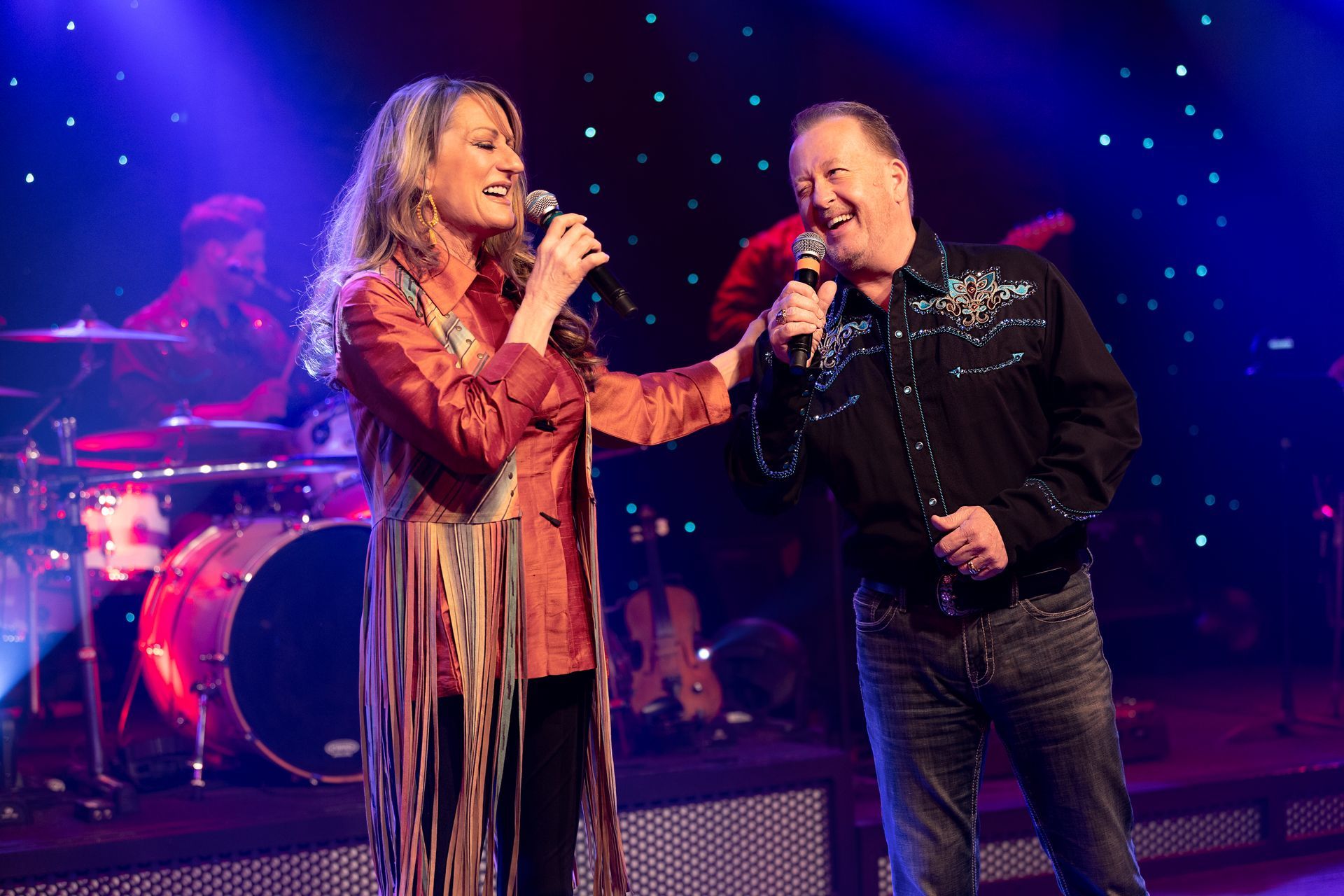 A man and a woman are singing into microphones on a stage.