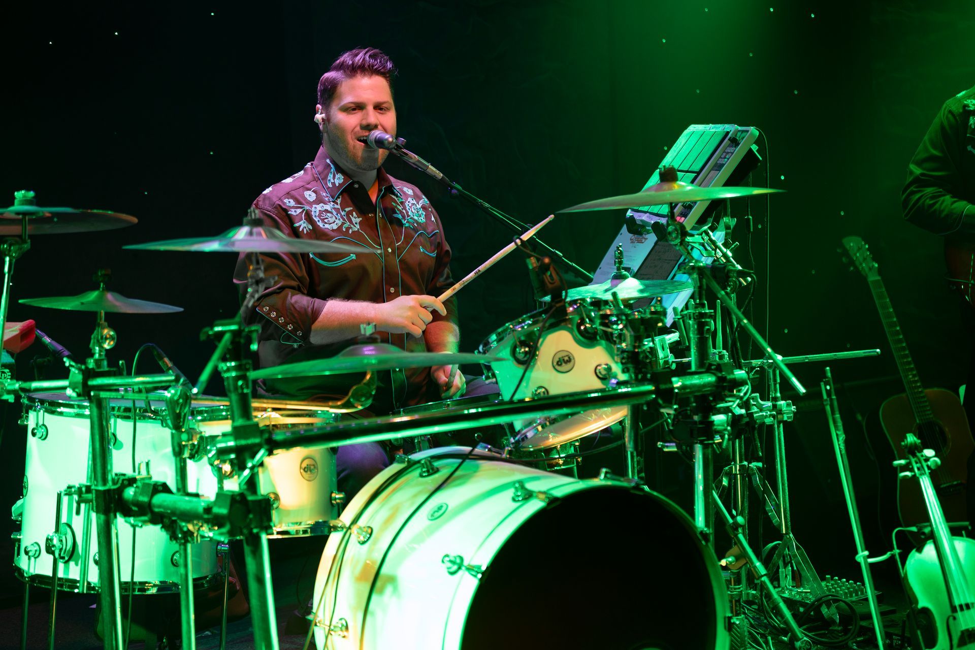 A man is playing drums and singing into a microphone on a stage.