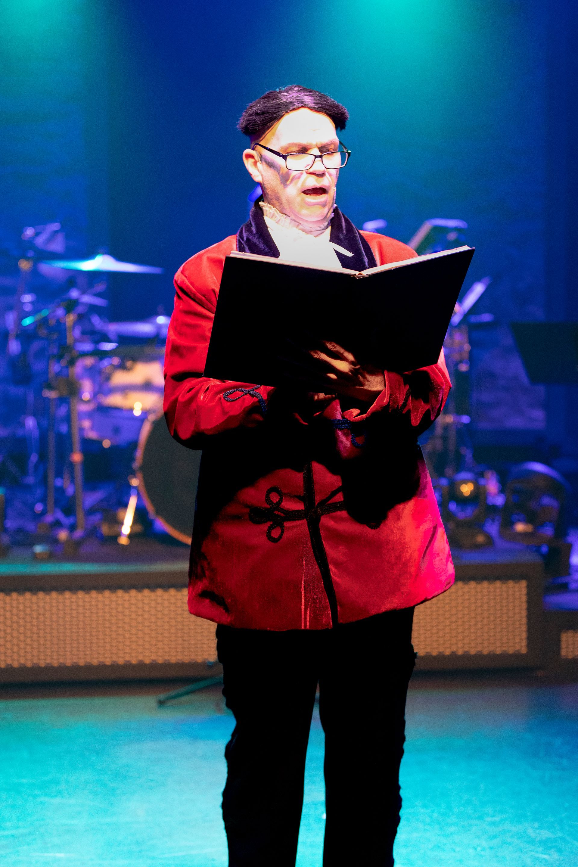 A man in a red coat is reading a book on a stage.