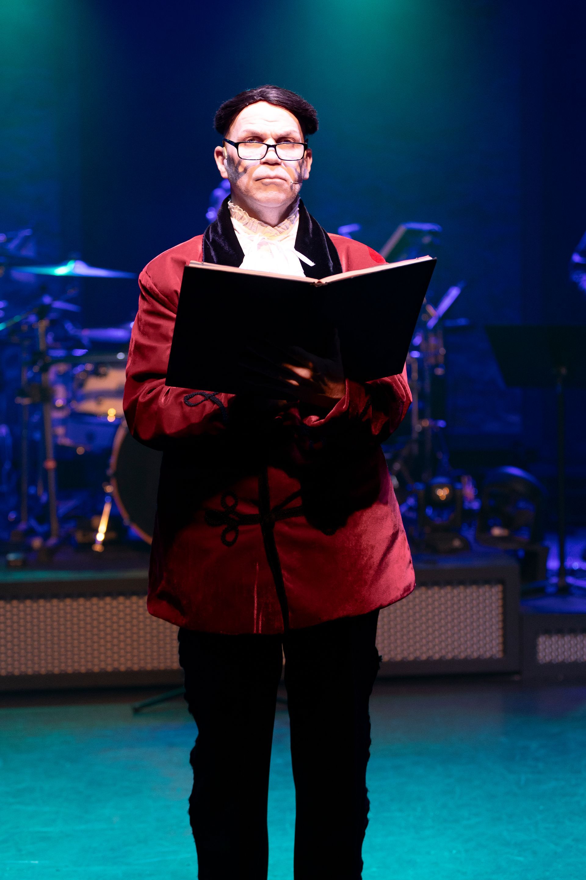 A man in a red jacket is standing on a stage holding a book.