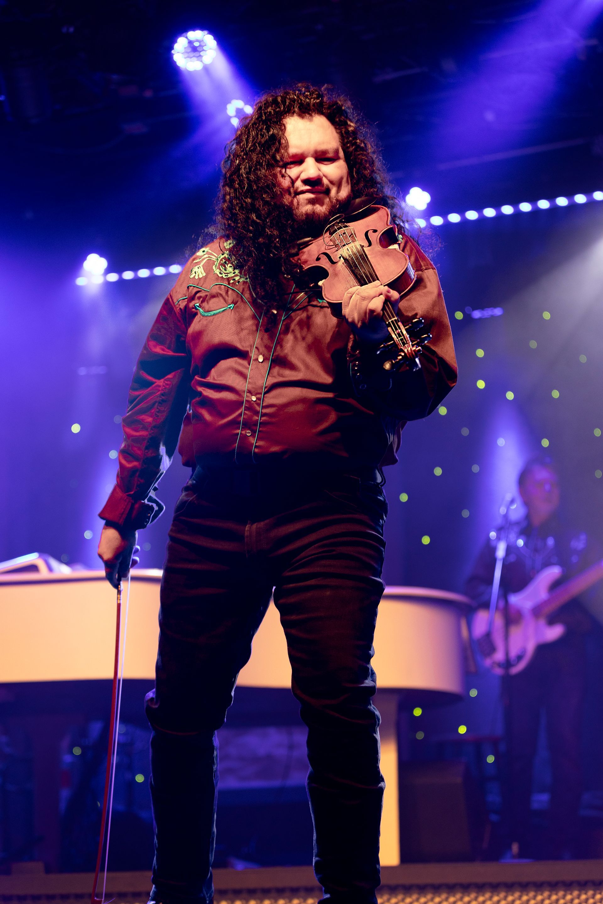 A man with long curly hair is standing on a stage holding a microphone.