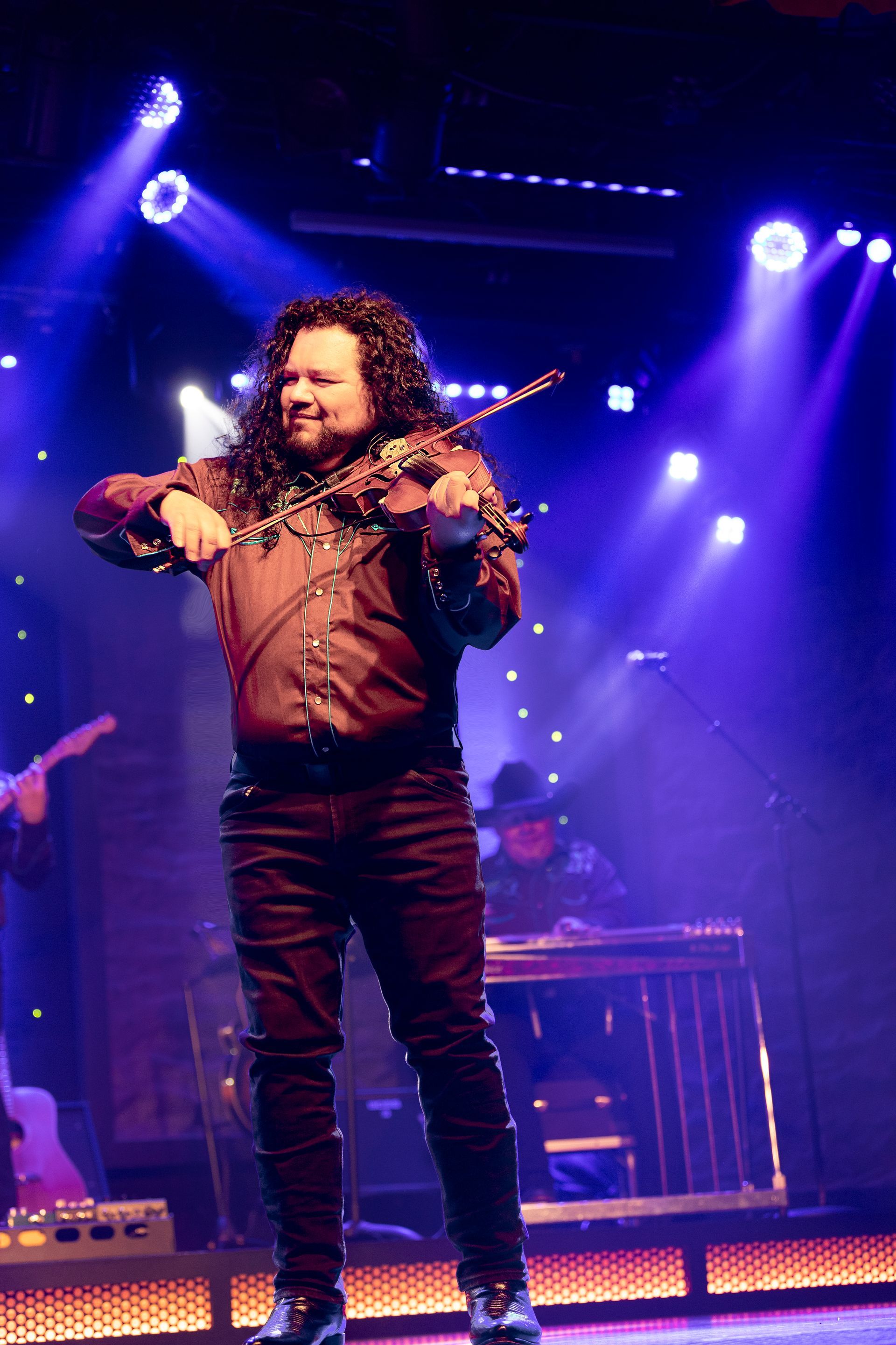 A man with long hair is playing a violin on a stage.