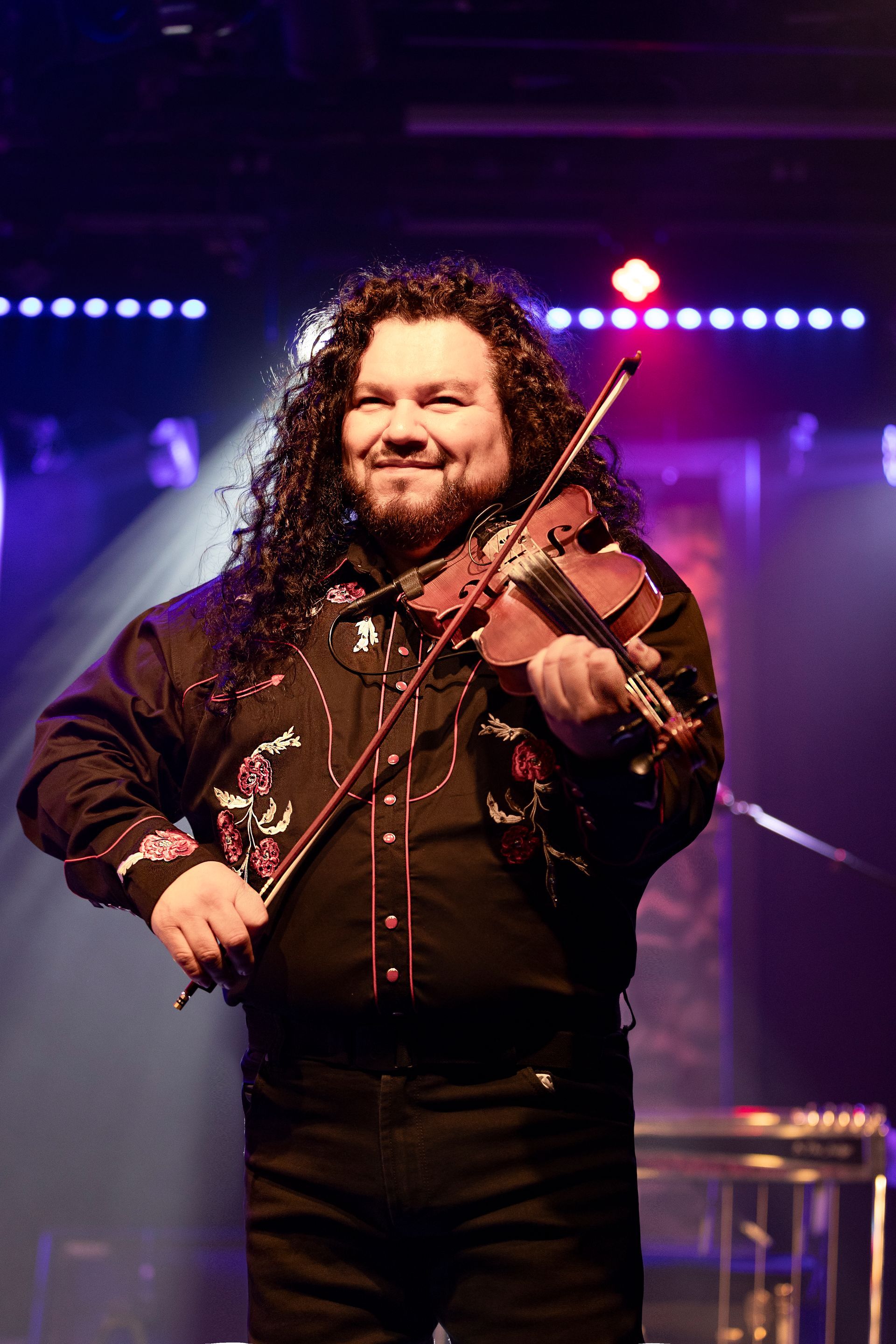 A man with long hair is playing a violin on a stage.
