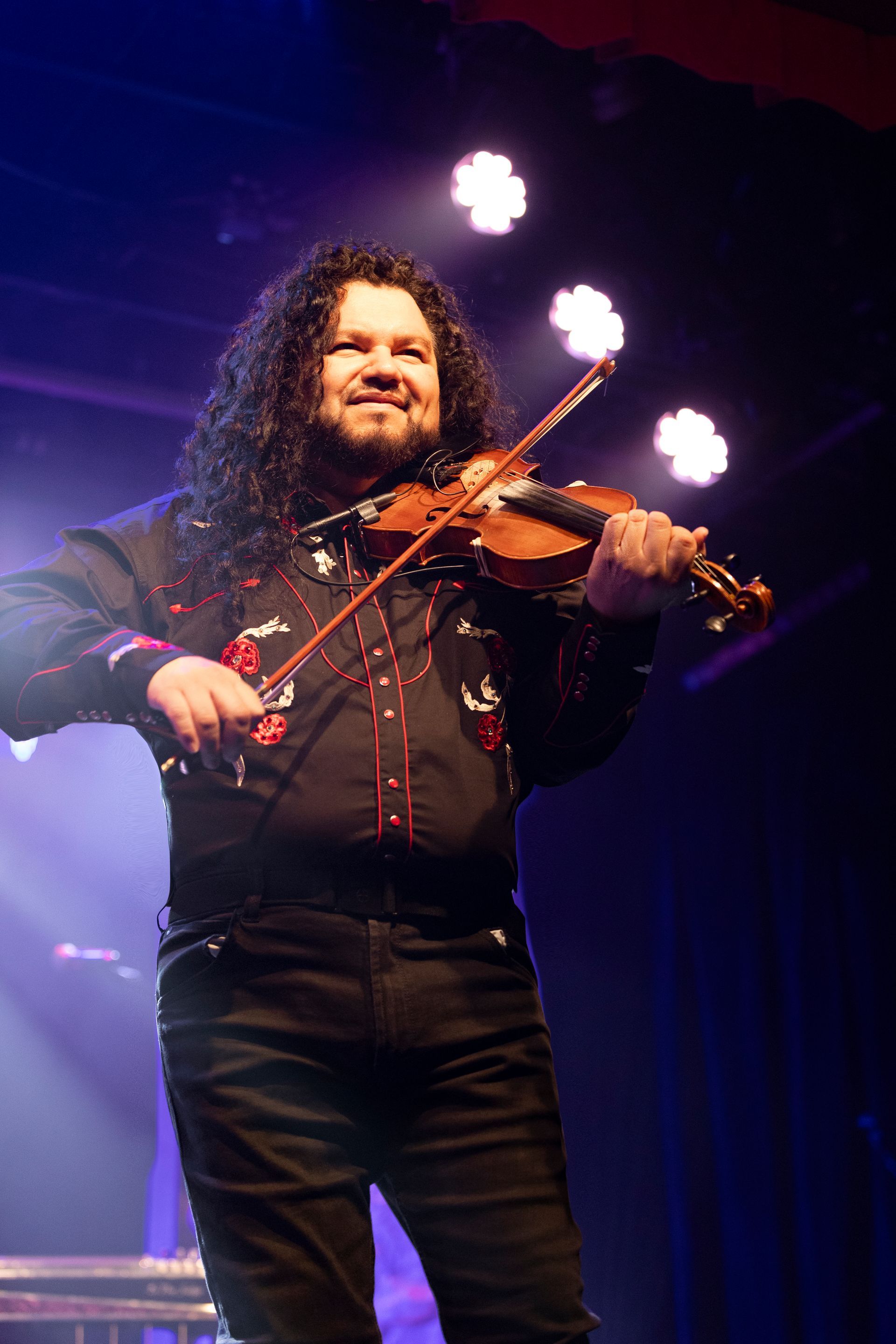 A man with long hair is playing a violin on a stage.