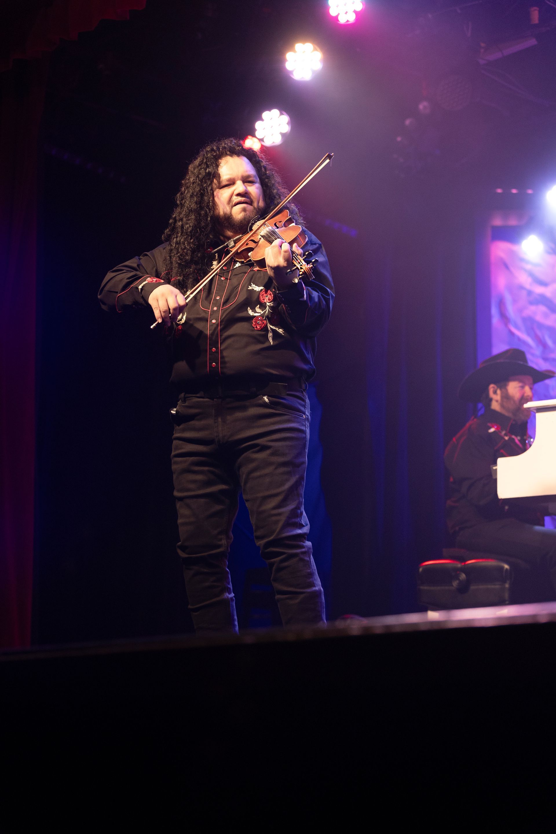 A man is playing a violin on stage while another man plays a piano.