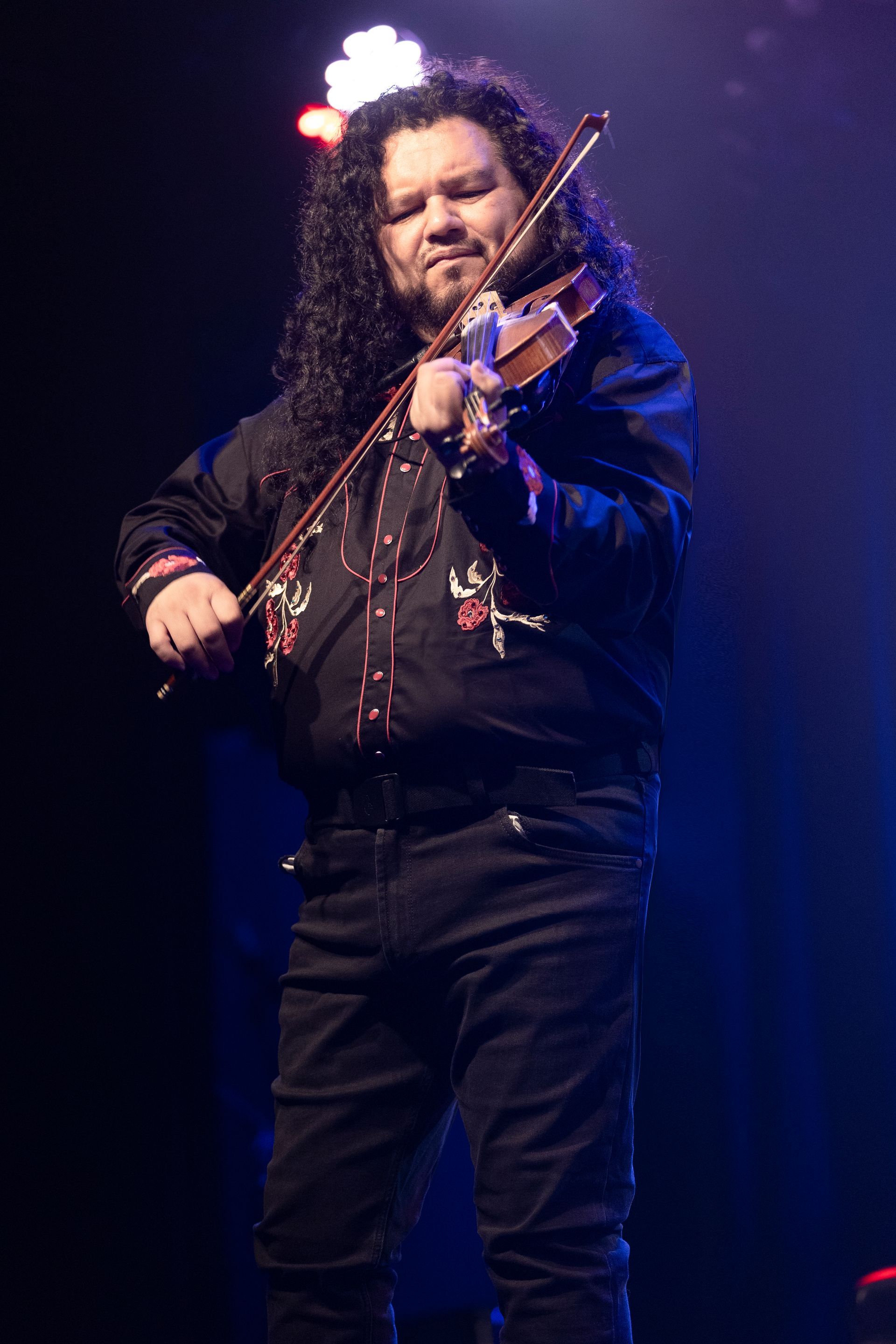 A man with long hair is playing a violin on a stage.