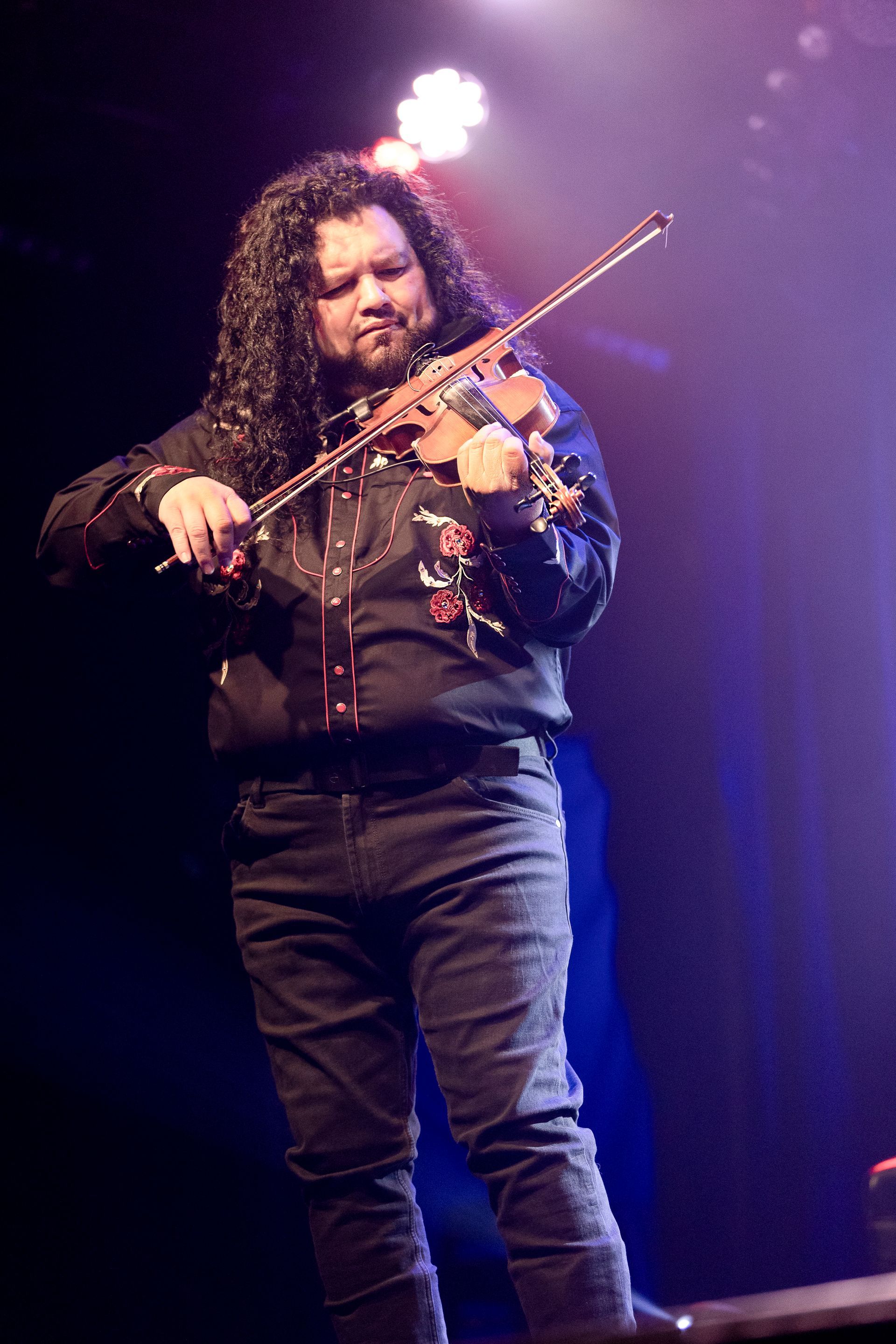 A man with long hair is playing a violin on a stage.
