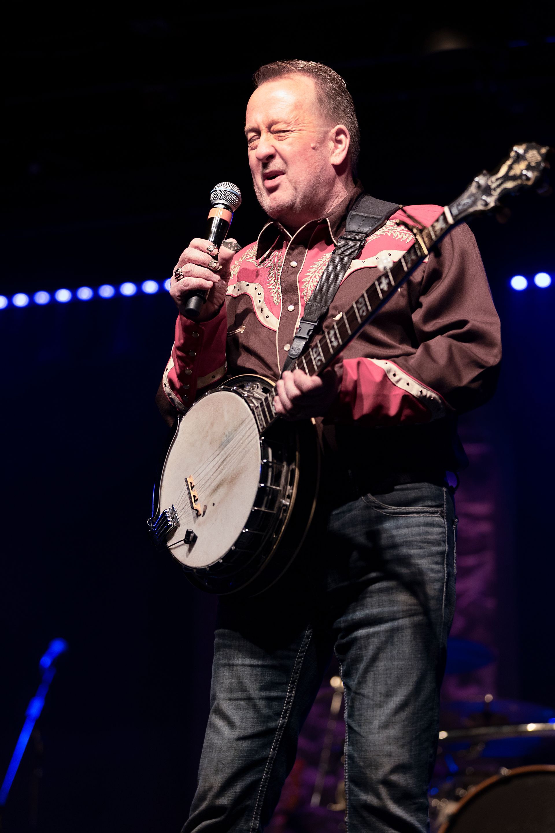 A man is playing a banjo and singing into a microphone on a stage.