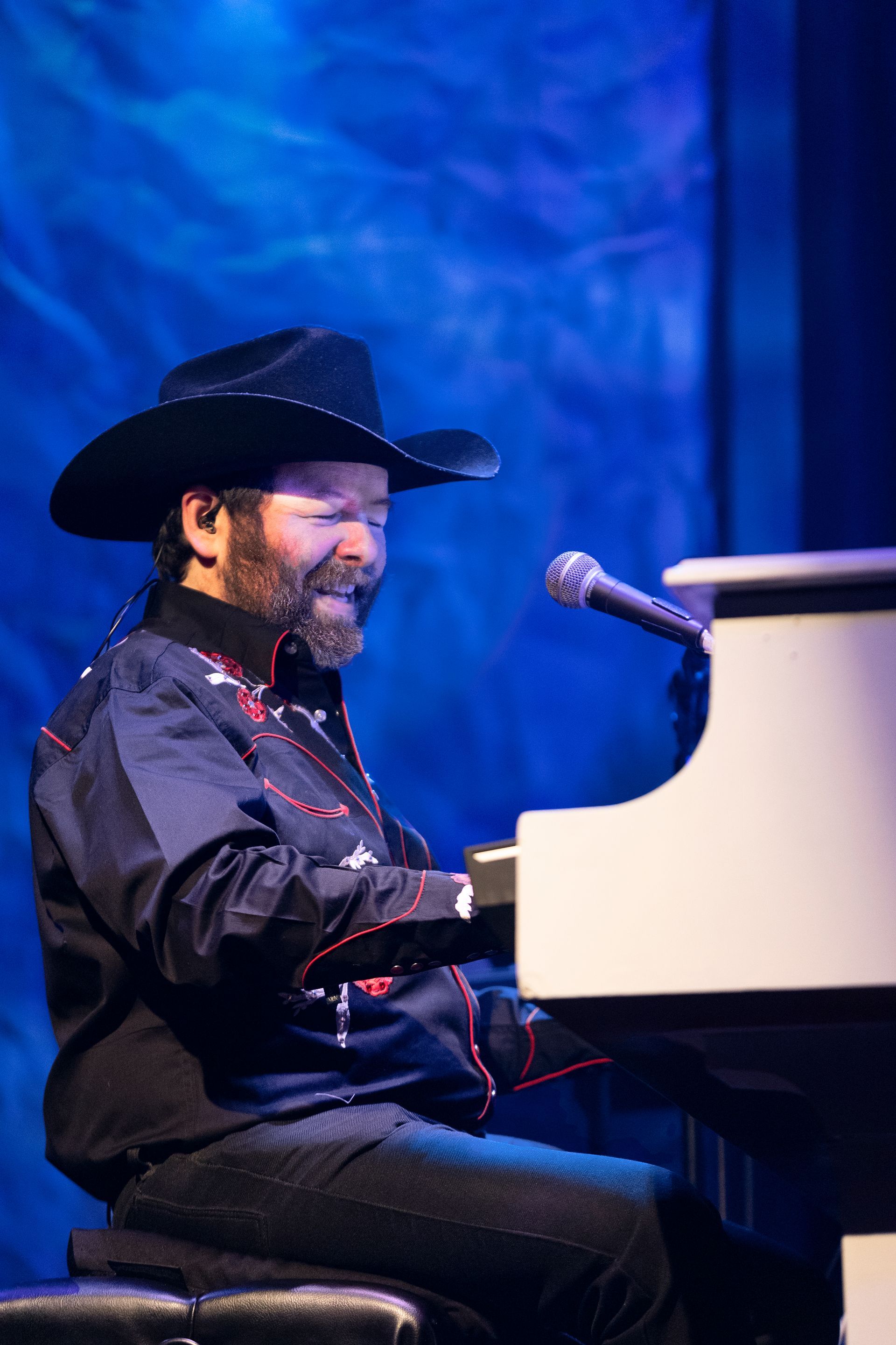 A man in a cowboy hat is playing a piano and singing into a microphone.