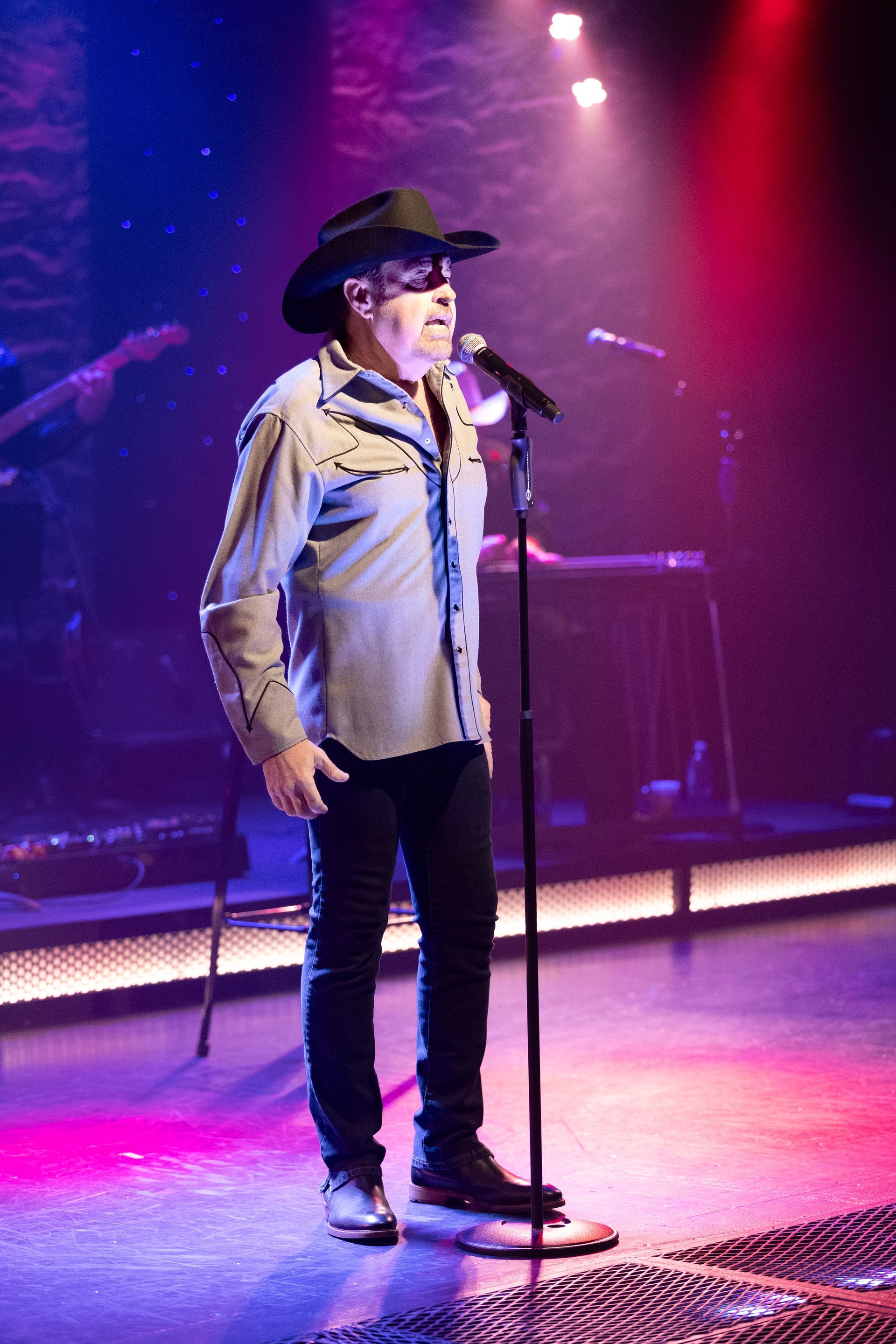 A man in a cowboy hat is singing into a microphone on a stage.