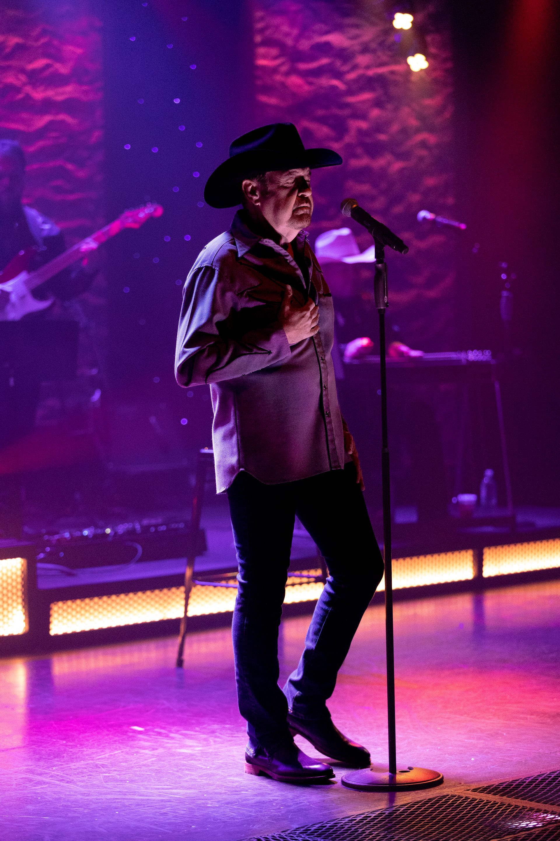 A man in a cowboy hat is singing into a microphone on a stage.