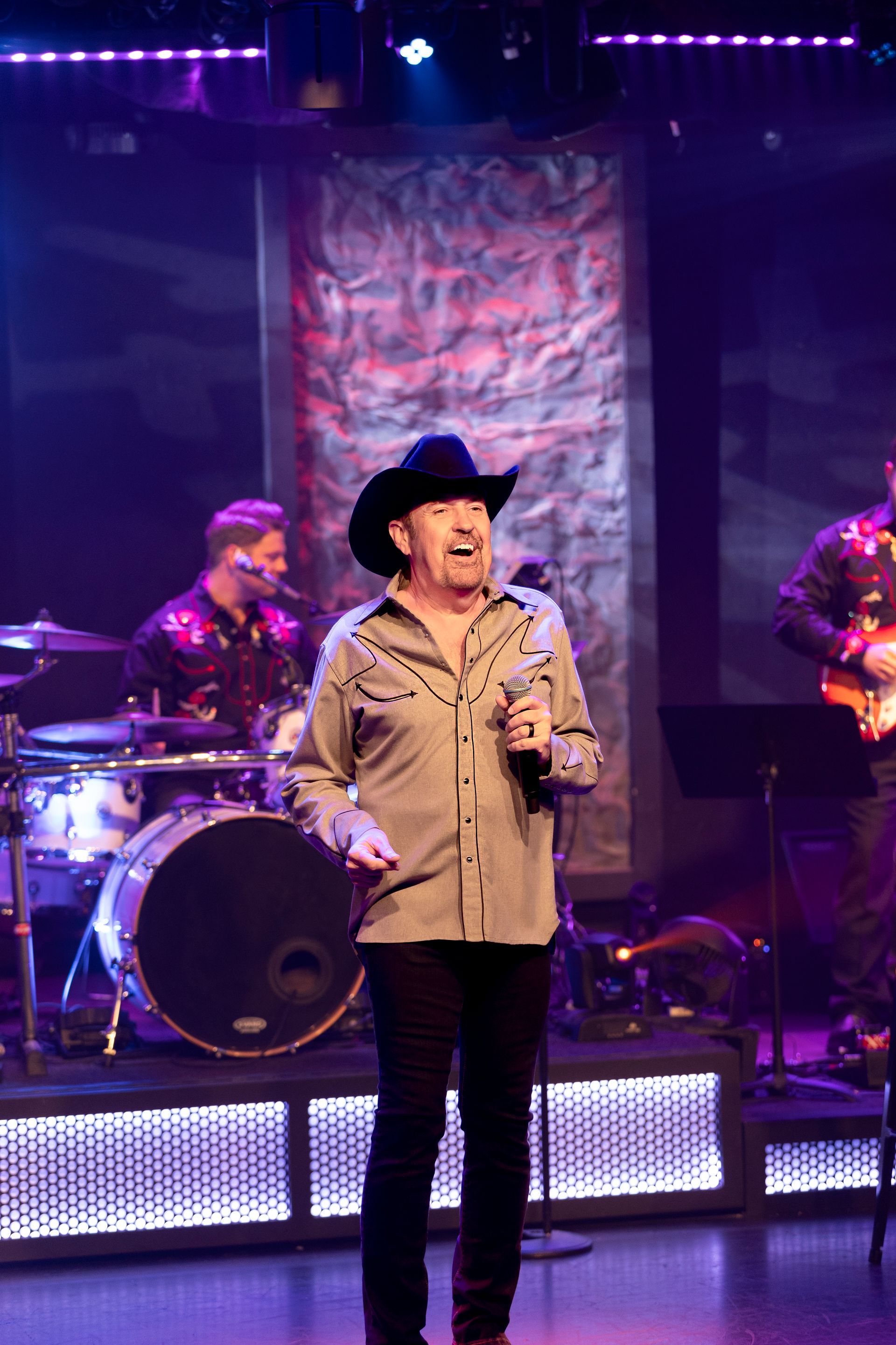 A man in a cowboy hat is singing into a microphone on a stage.