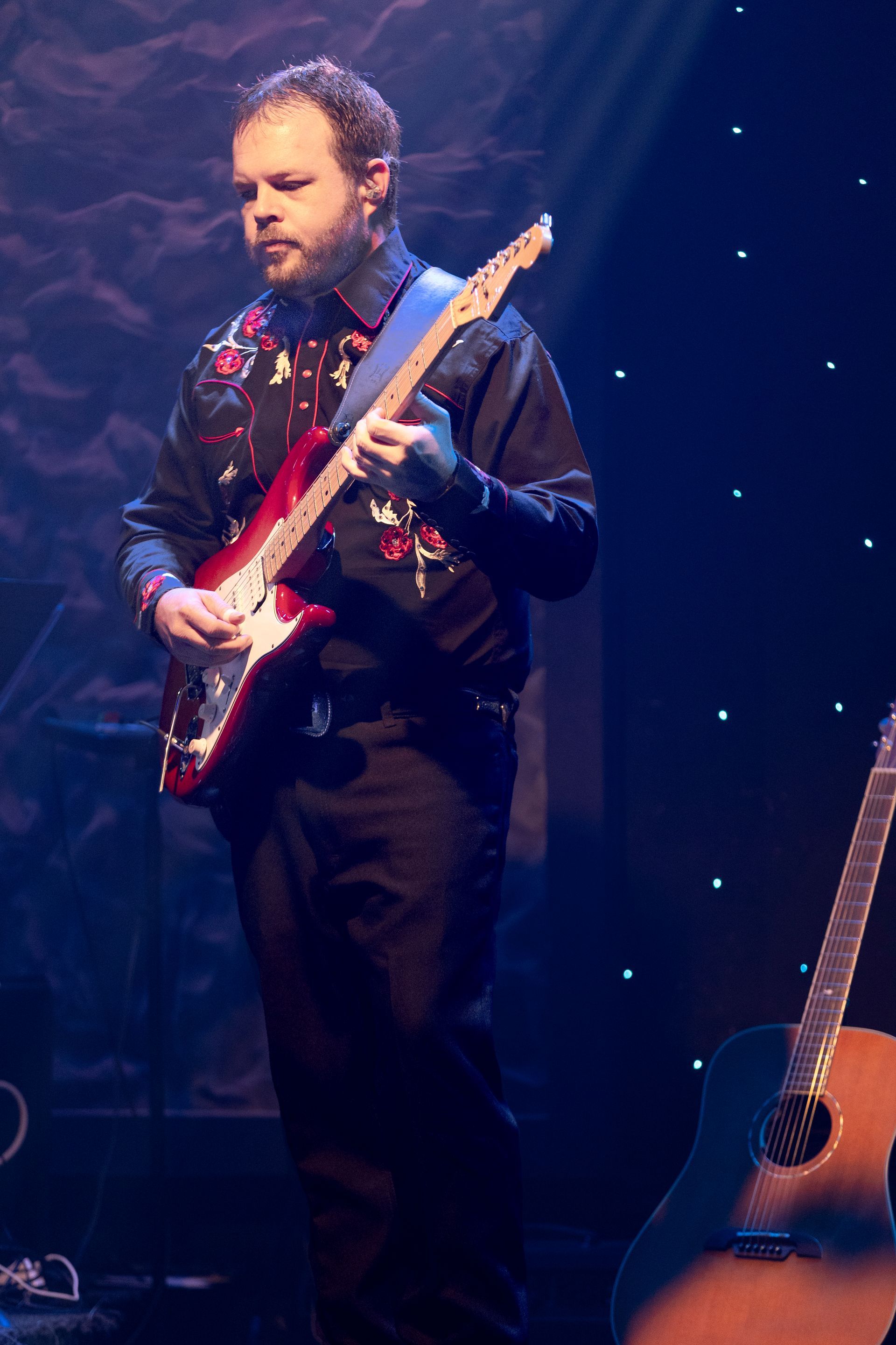 A man is playing a red electric guitar on a stage.