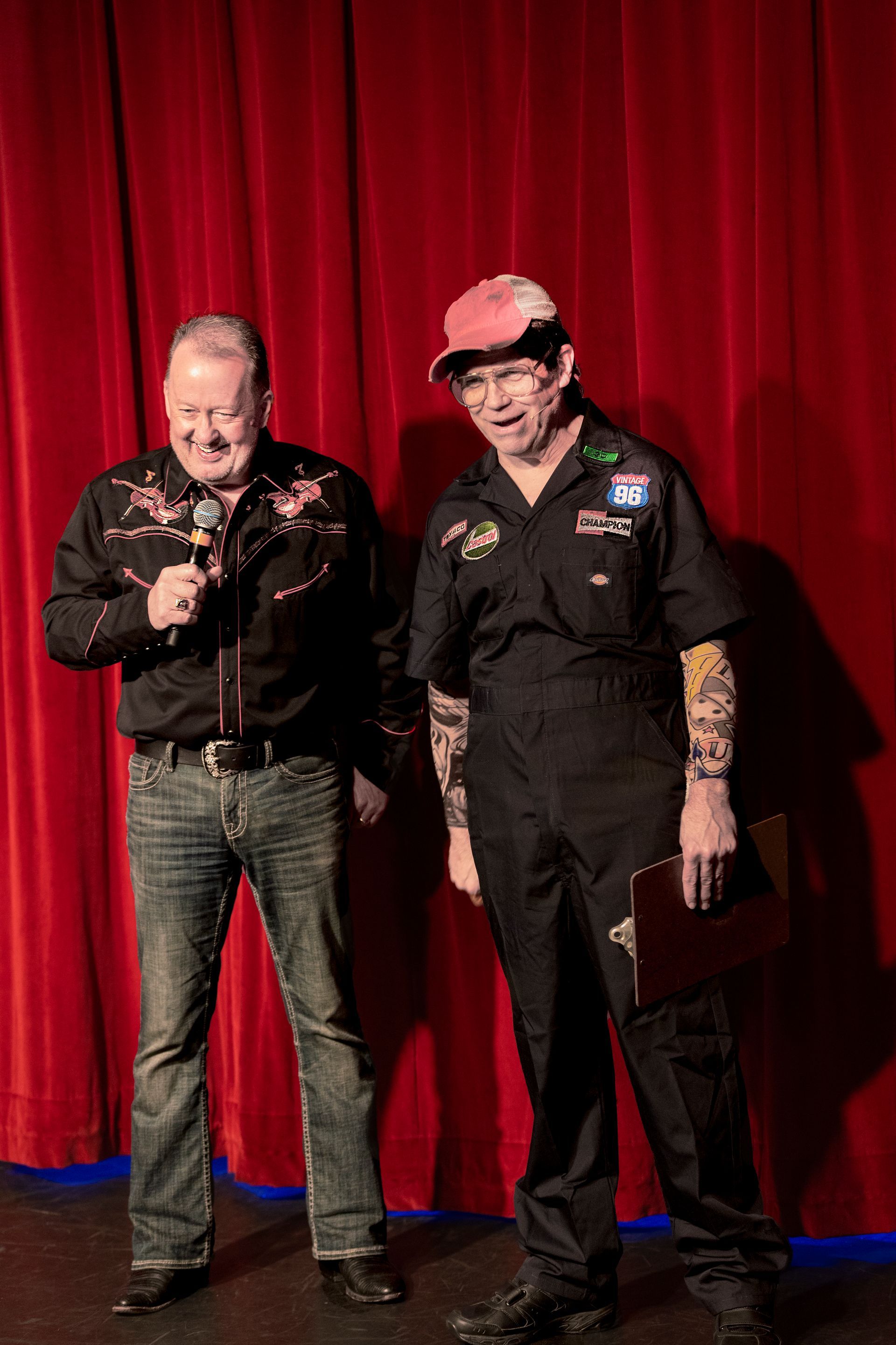 Two men are standing next to each other on a stage in front of a red curtain.