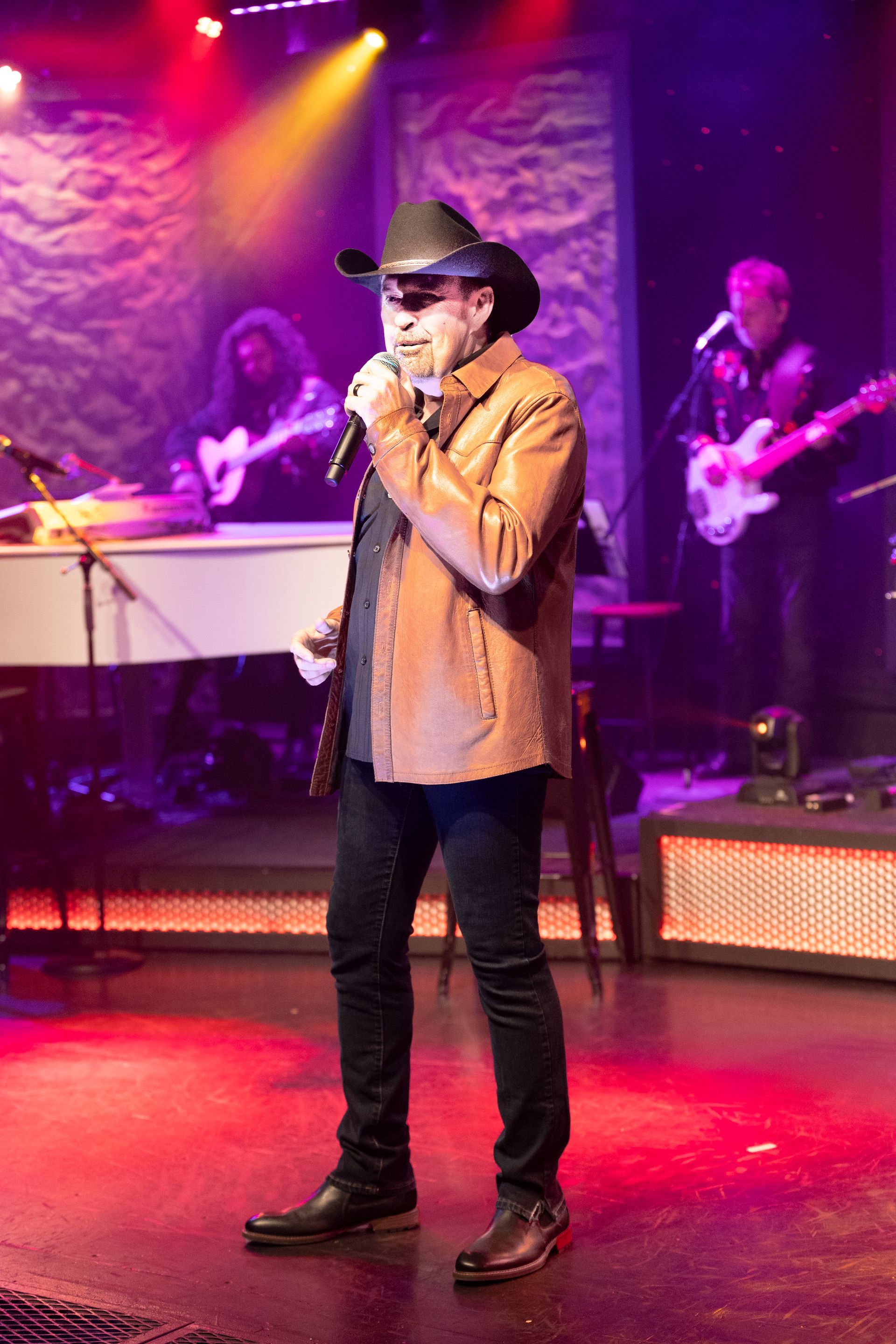A man in a cowboy hat is singing into a microphone on a stage.