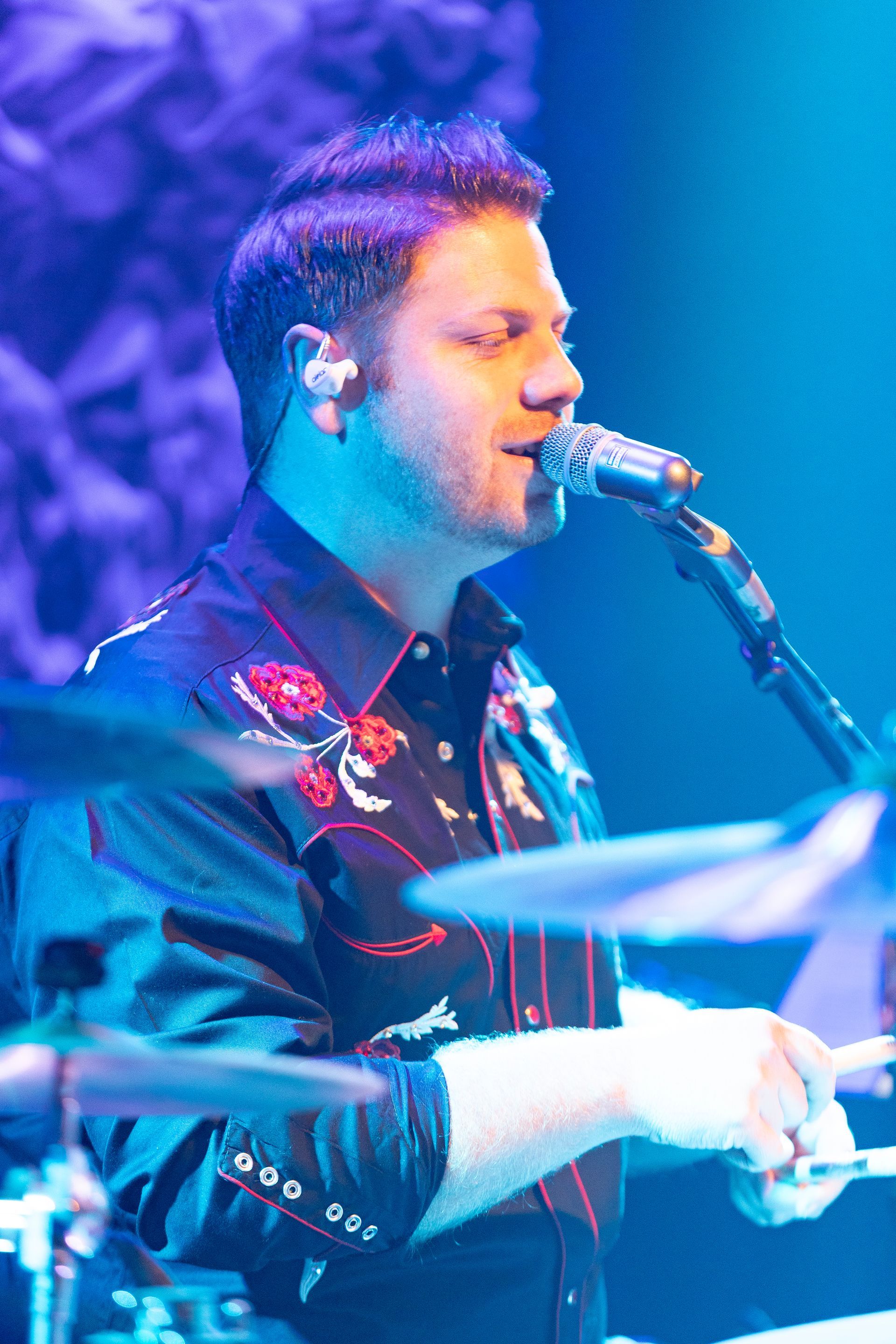 A man is singing into a microphone while playing drums.