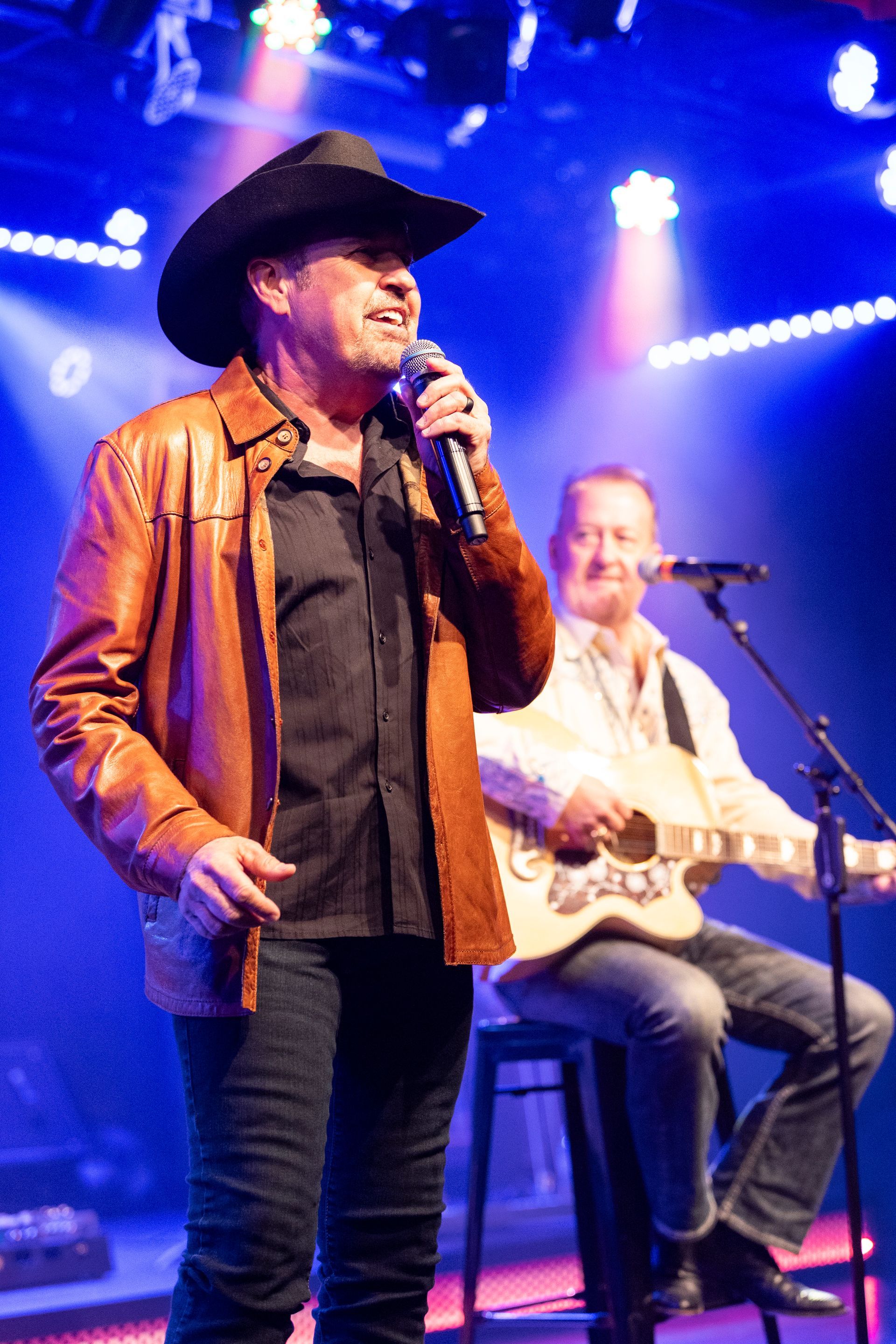 A man in a cowboy hat is singing into a microphone on stage