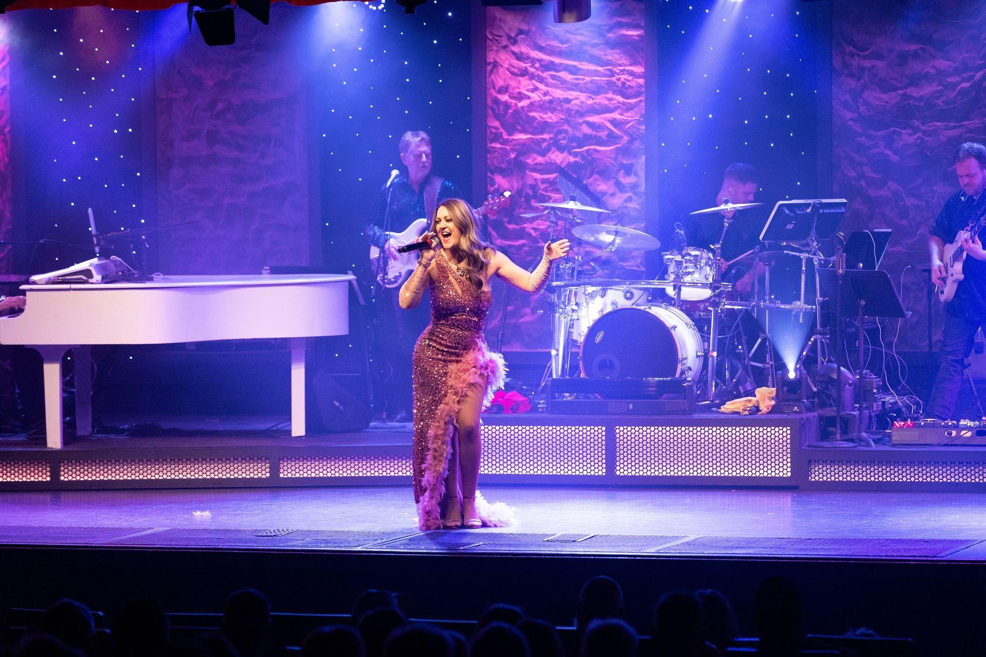 A woman is singing on a stage with a piano in the background.