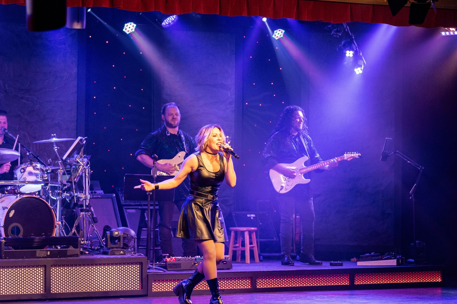 A woman is singing into a microphone on a stage in front of a band.