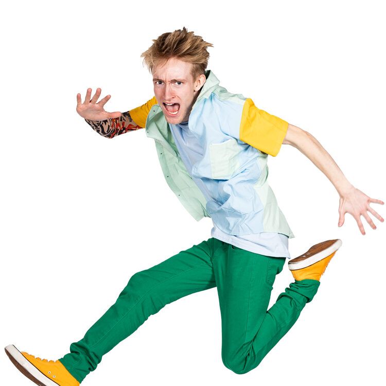 A young man in a blue shirt and green pants is jumping in the air