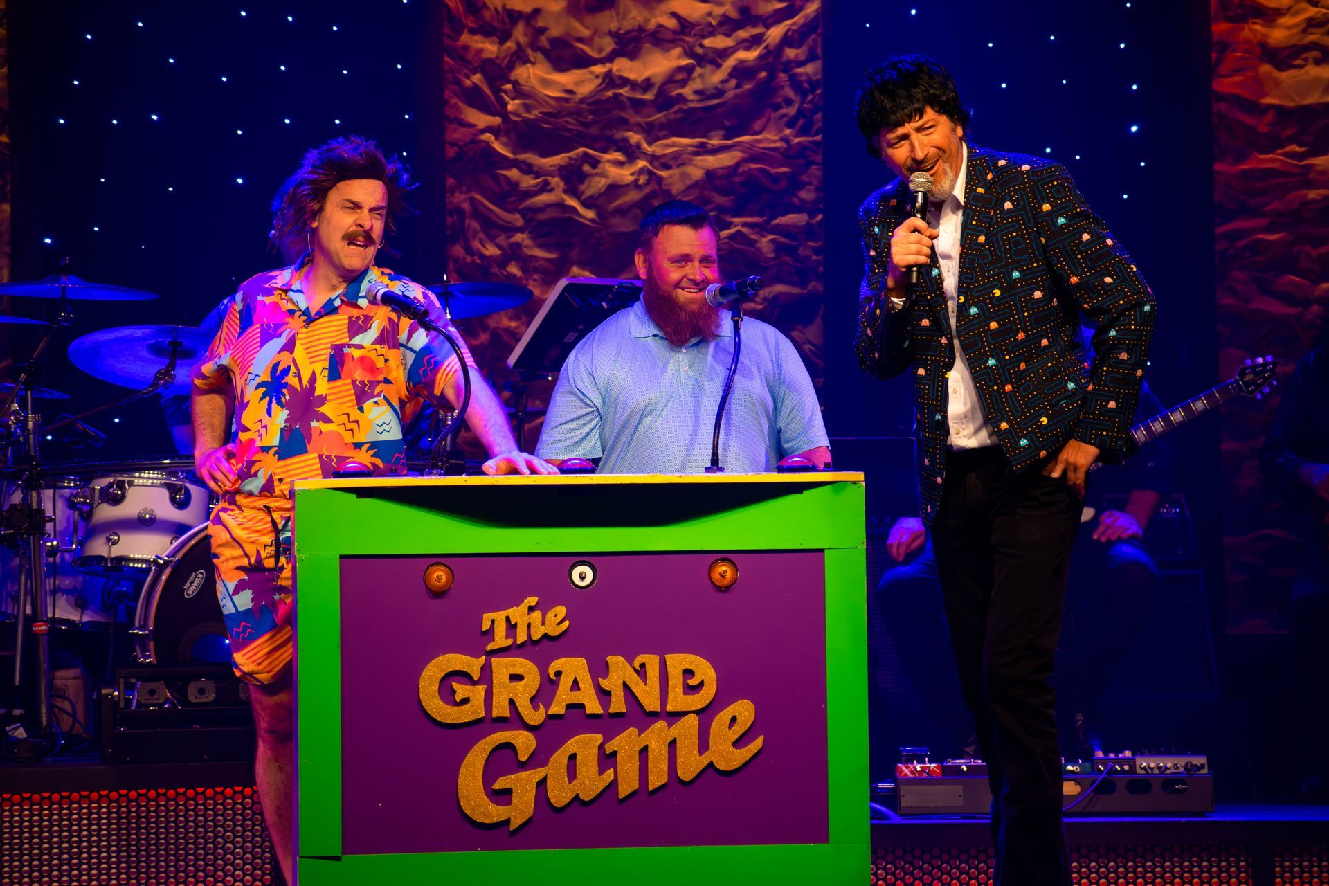 A group of people are standing around a green box that says the grand game.