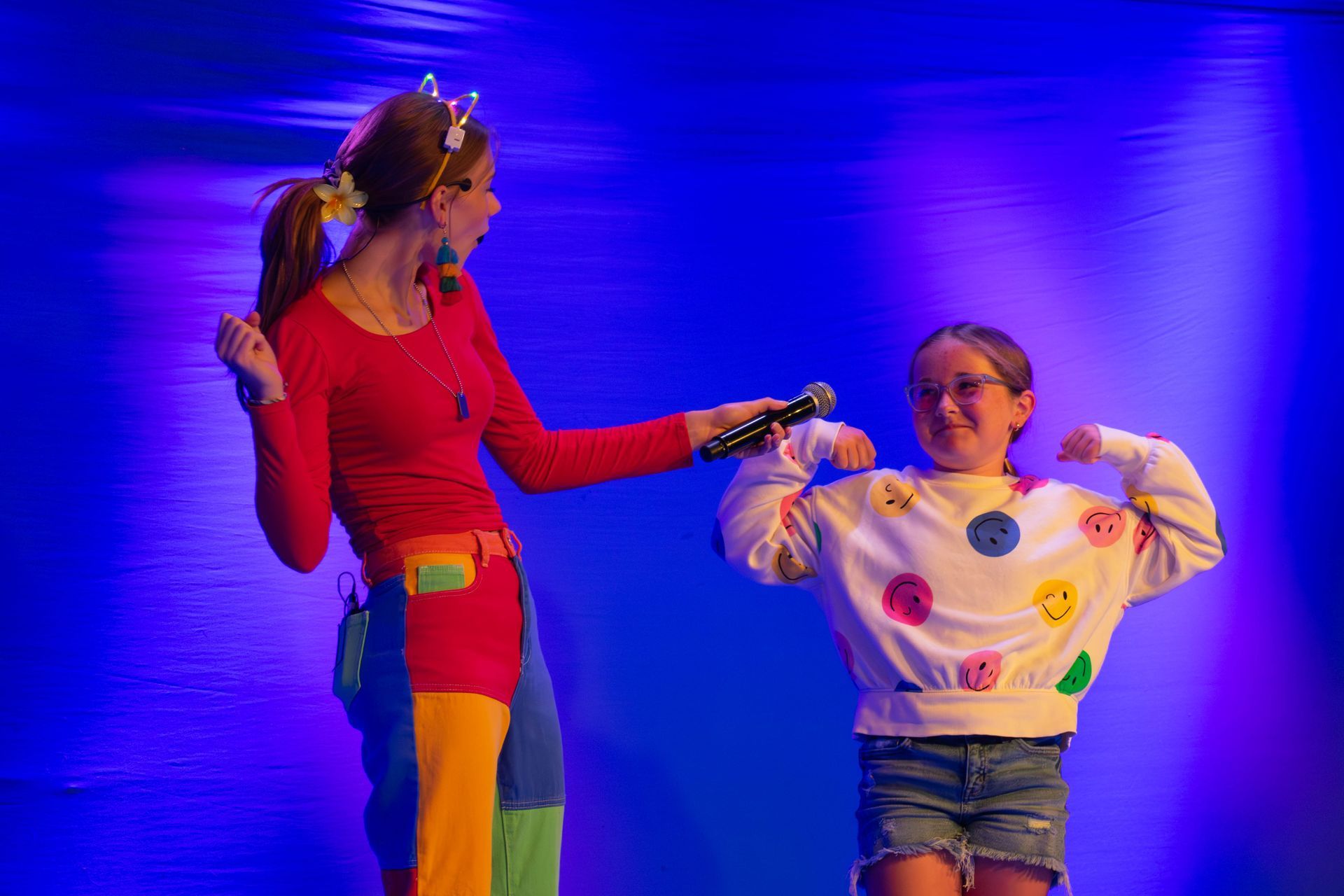 A woman is holding a microphone next to a young girl on a stage.