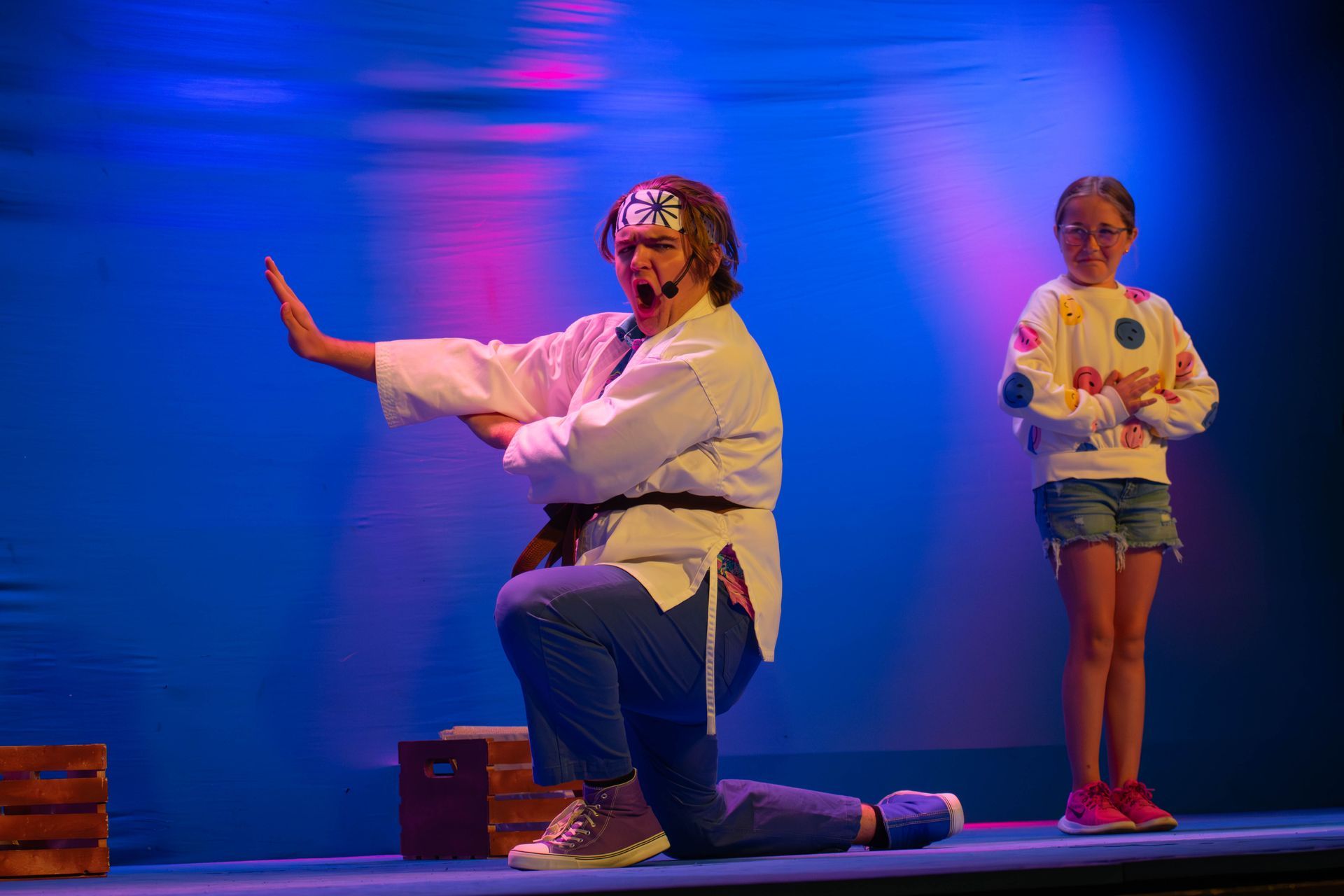 A woman in a karate uniform is kneeling on a stage next to a little girl.
