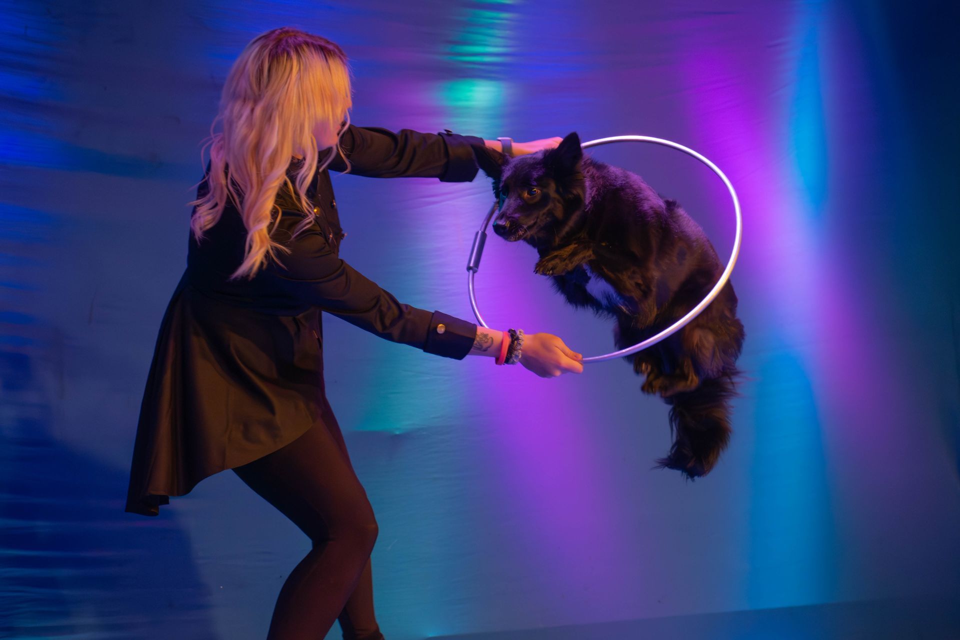 A woman is holding a hula hoop around a black dog.