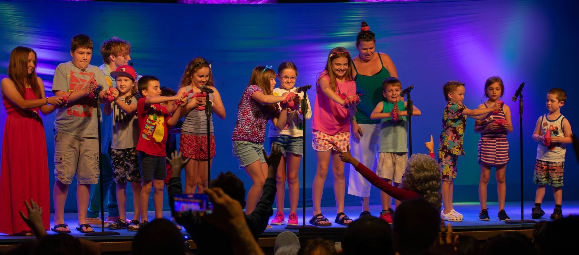A group of children are singing into microphones on a stage.