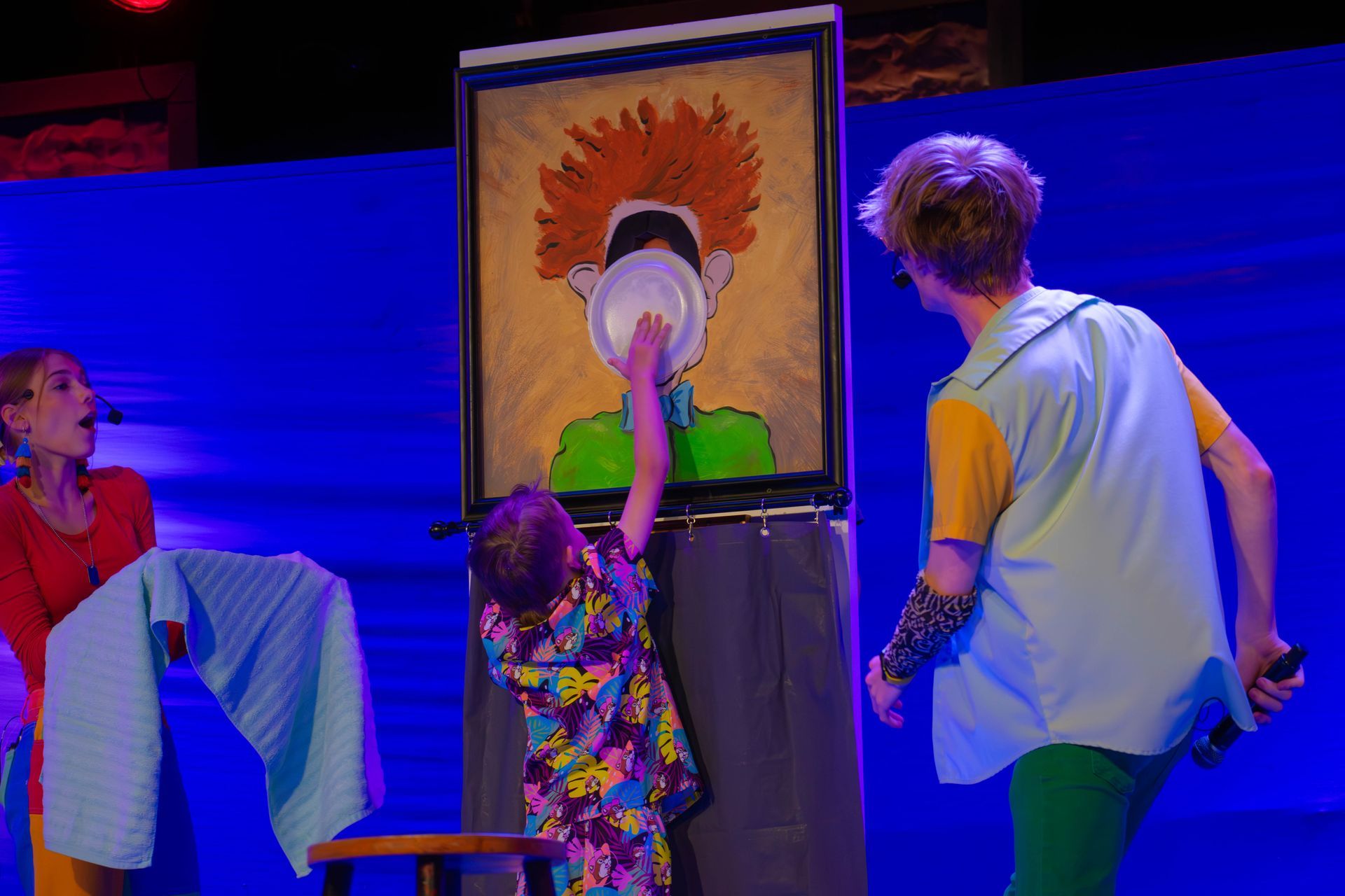A group of people are standing in front of a painting of a man with red hair.