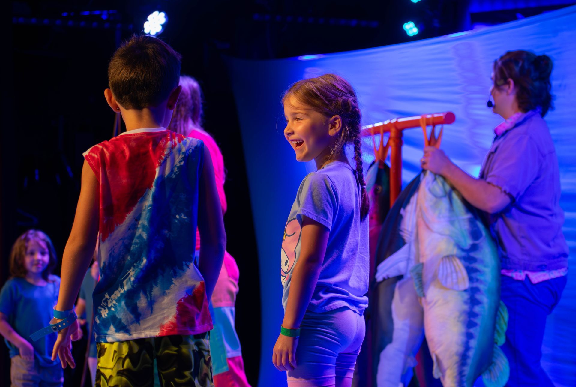 A group of children are standing on a stage holding stuffed fish.