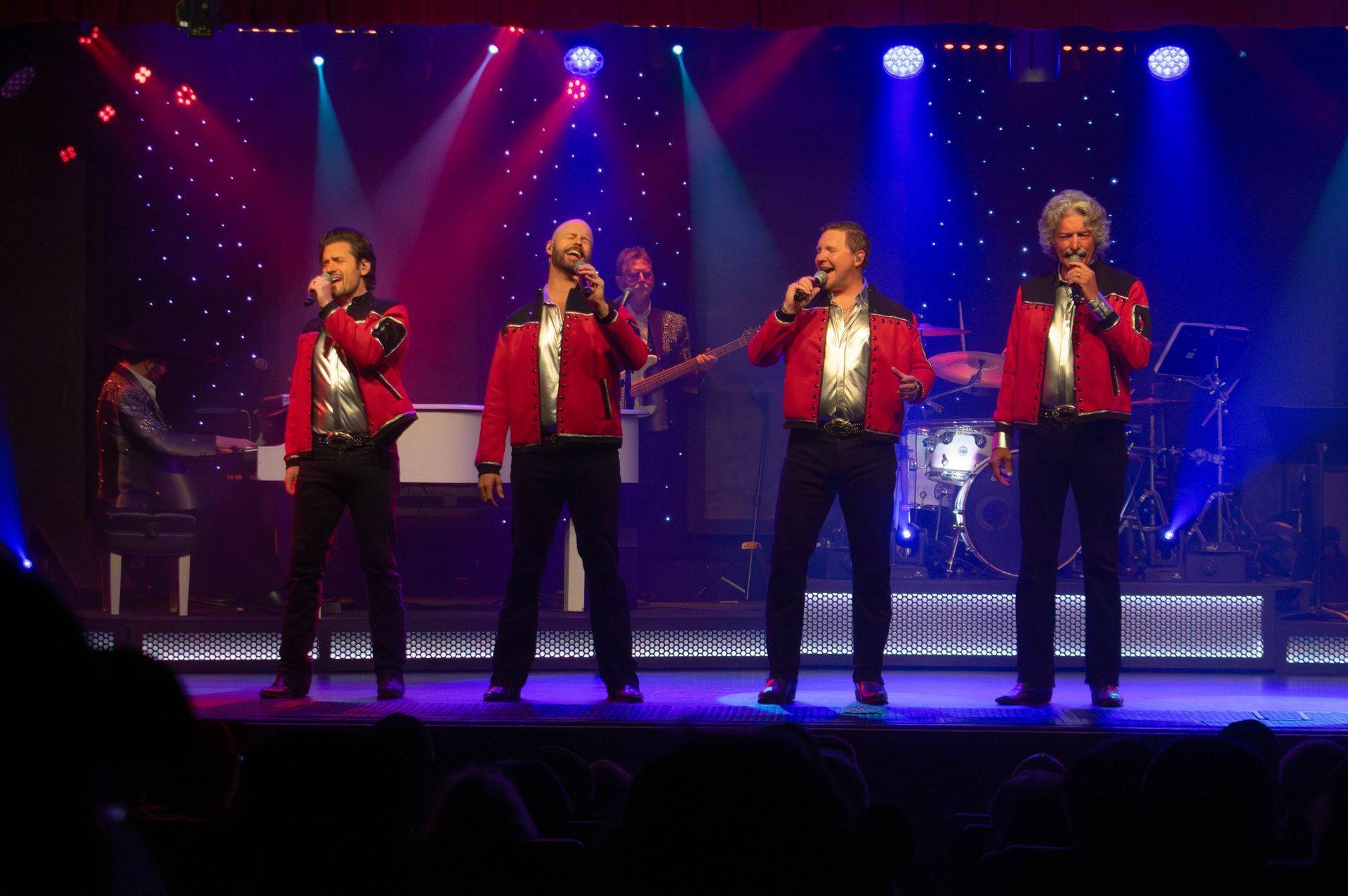 Two men on a stage with microphones. One wears an orange plaid blazer, while the other wears a dark blue suit.
