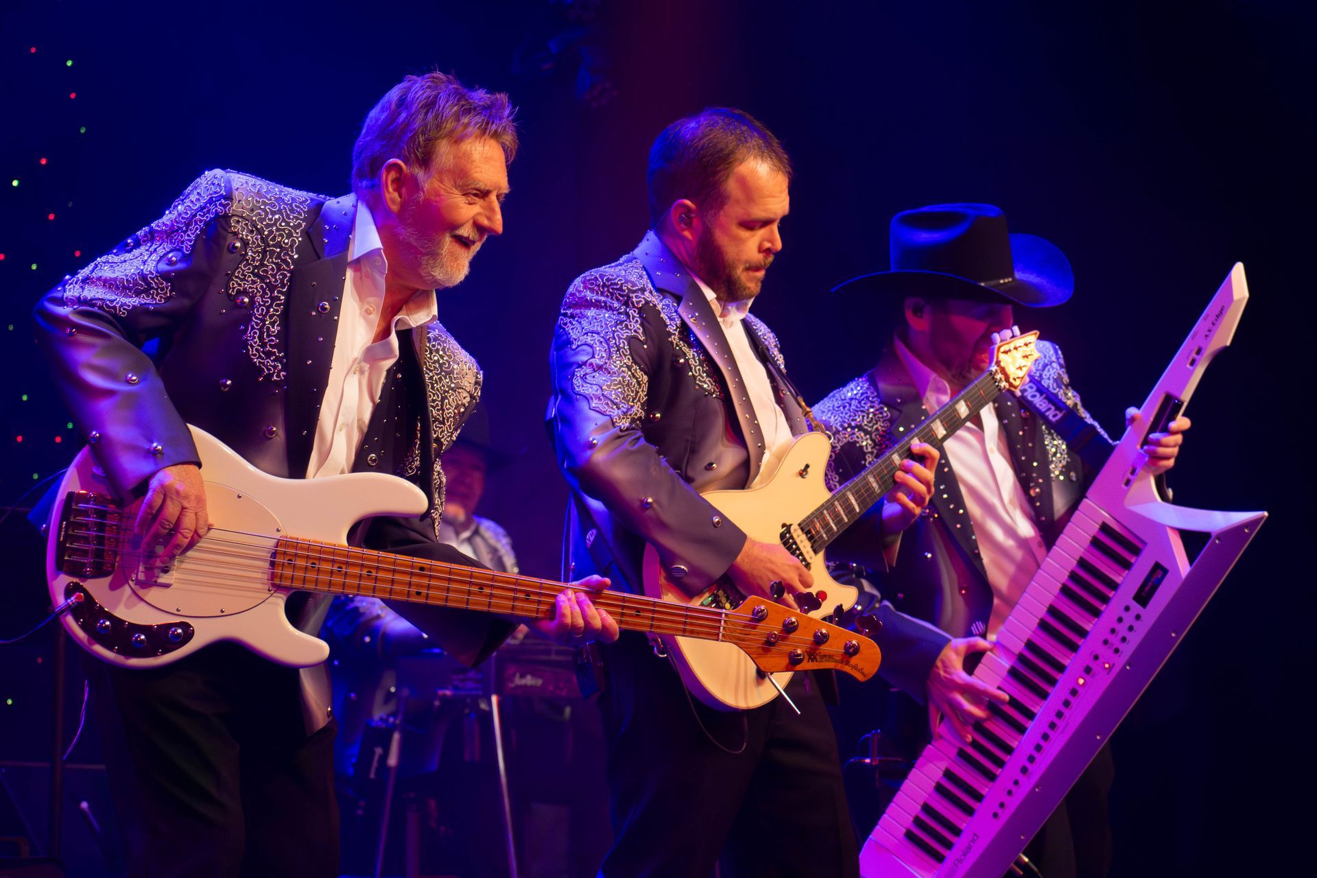 A man in a cowboy hat is singing into a microphone while playing a piano