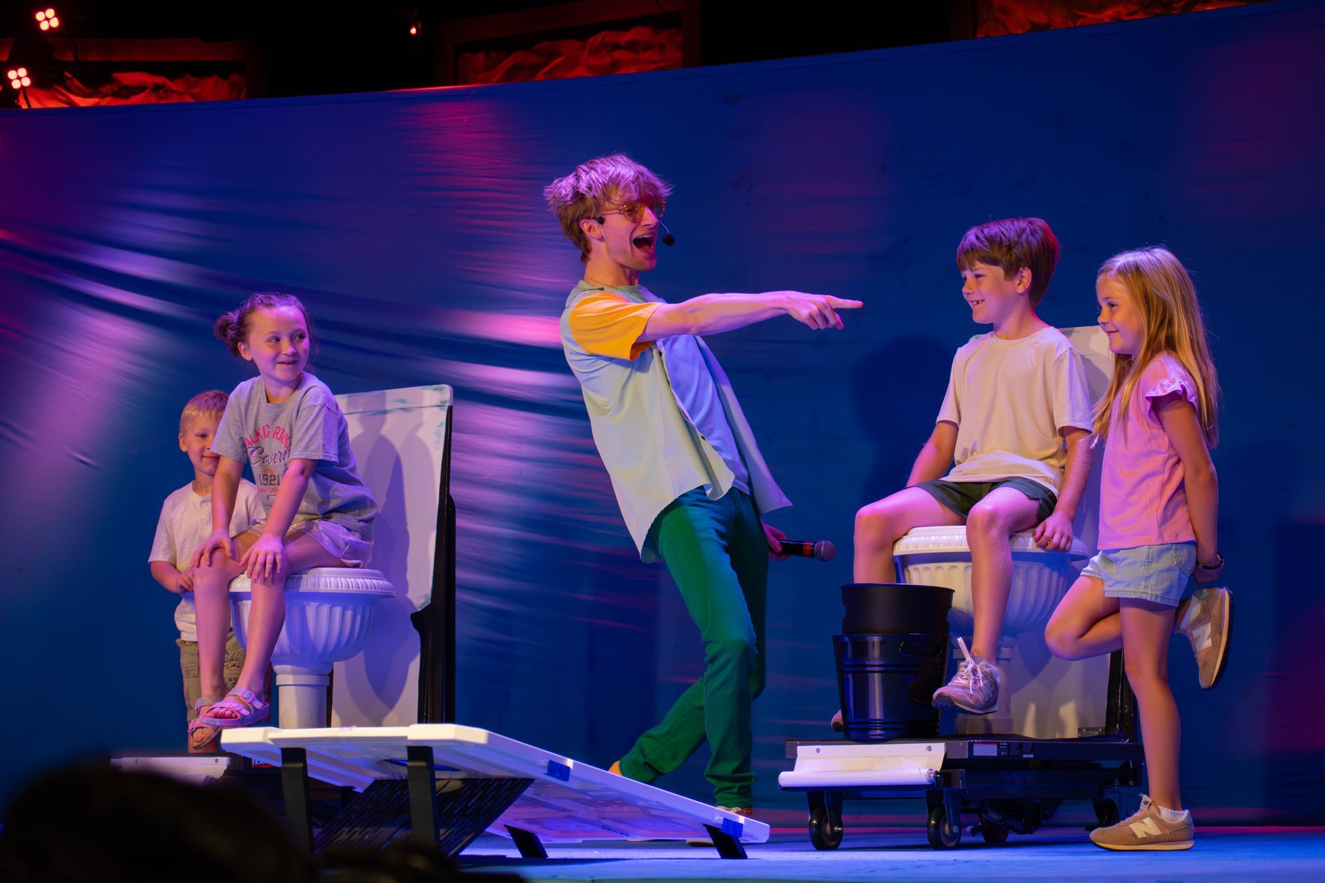 A group of children are sitting on a toilet on a stage.