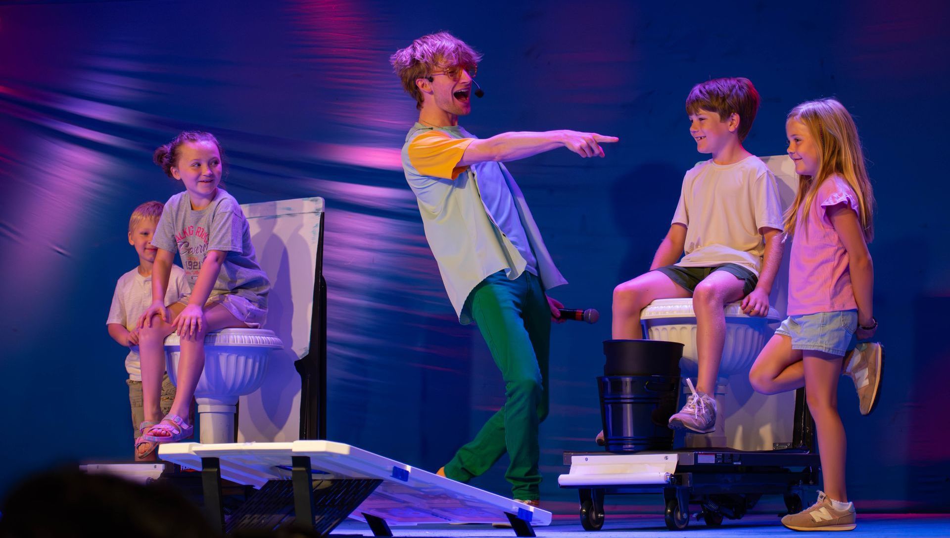 A group of children are sitting on toilets on a stage.