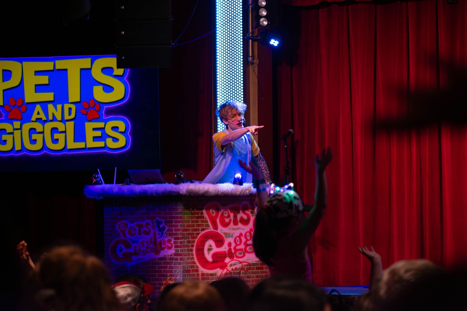 A man is standing on a stage in front of a sign that says pets and giggles.