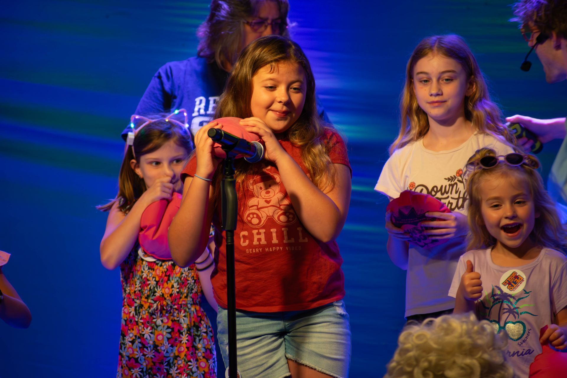 A group of young girls are singing into a microphone on a stage.