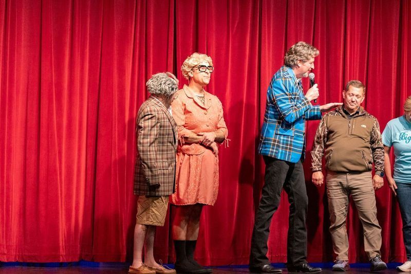 A group of people are standing on a stage in front of a red curtain.
