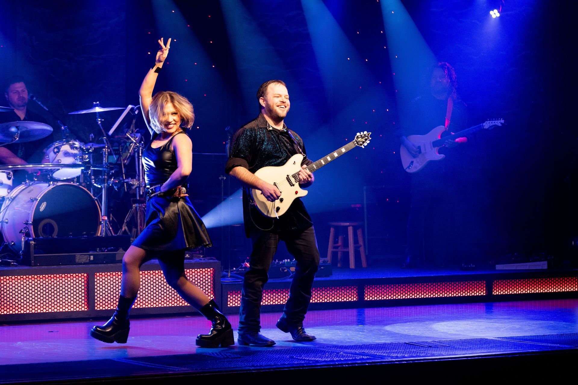 A man and a woman are standing on a stage playing guitars.