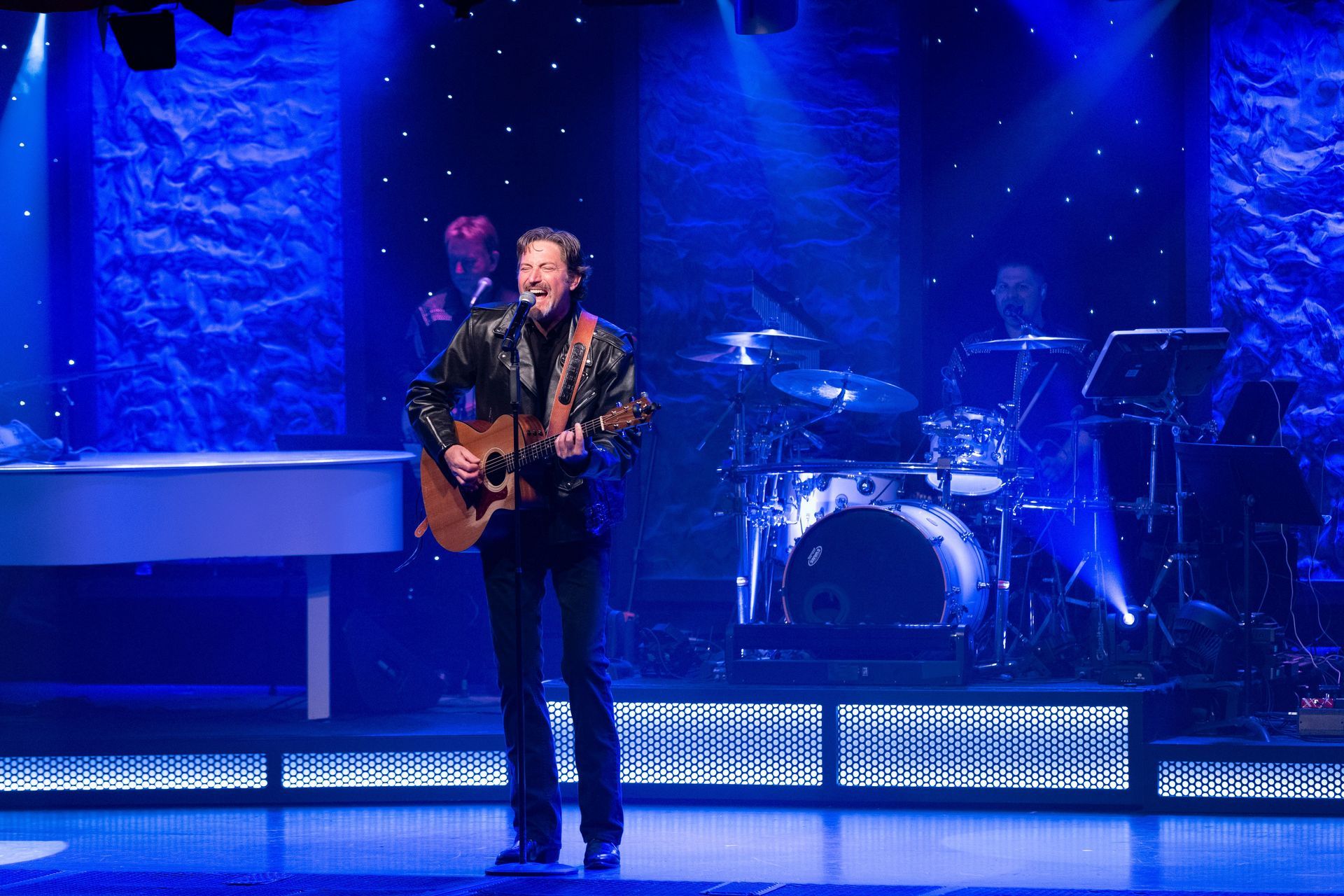 A man is playing a guitar and singing into a microphone on a stage.