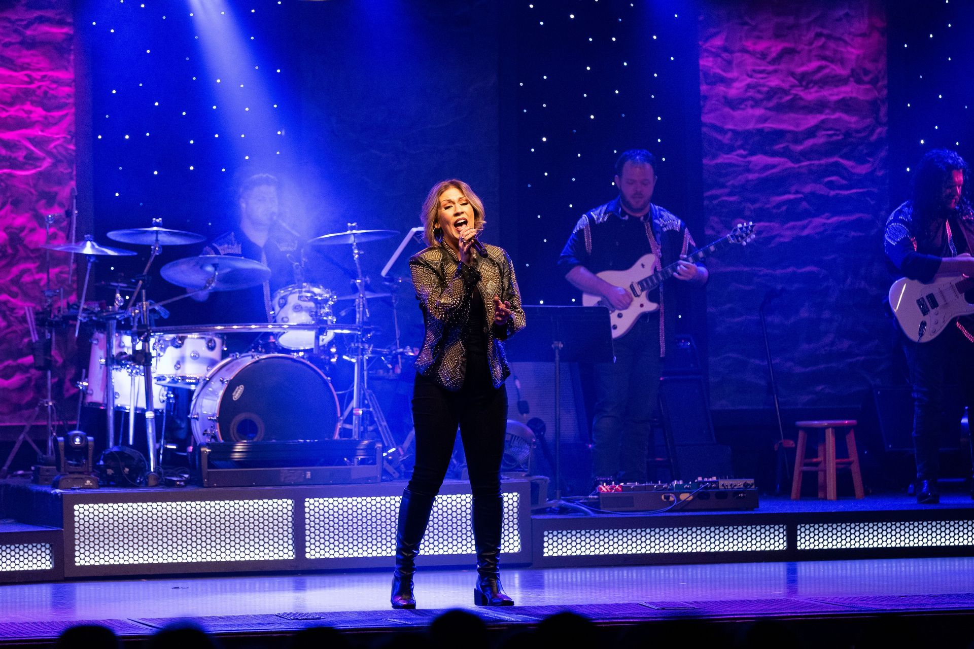 A woman is singing on a stage in front of a band.