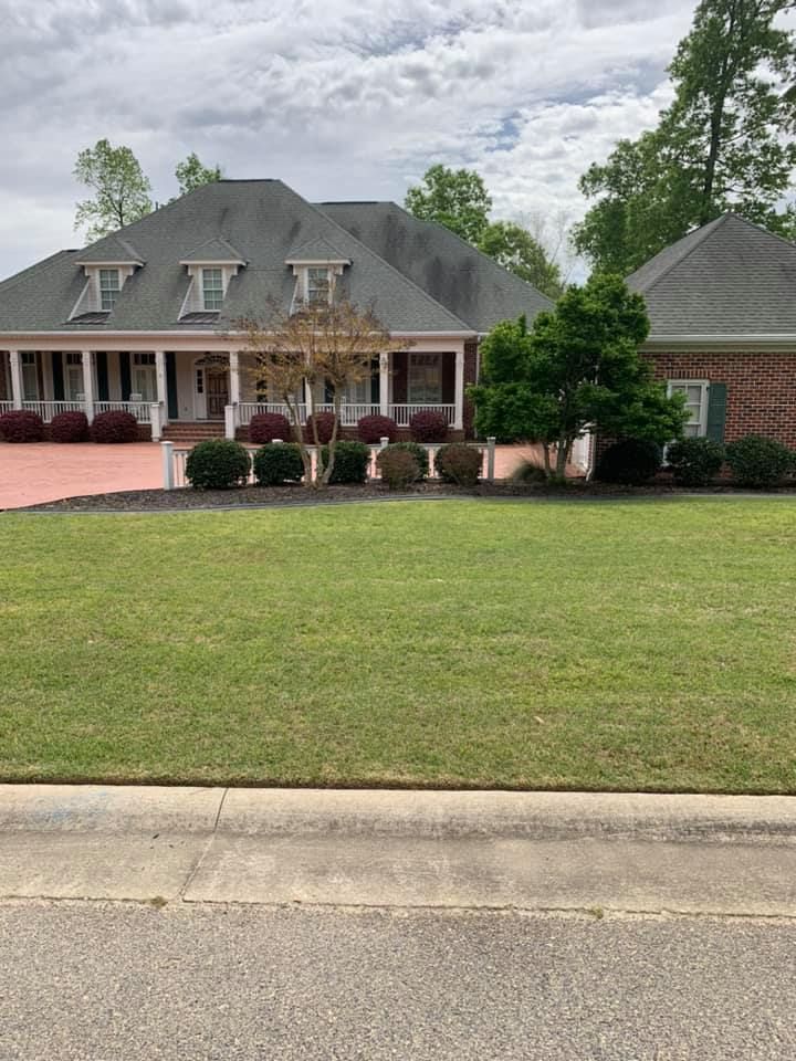 Large brick house with a green lawn, red-bricked pathway, and cloudy sky.