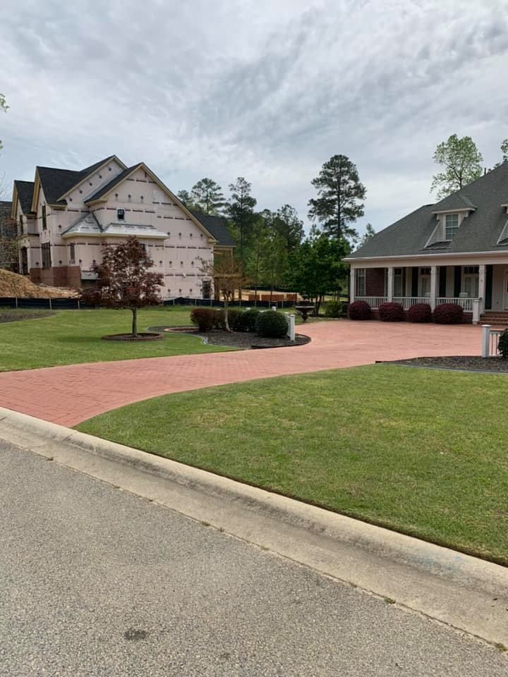 New houses, one under construction, red driveway, green grass, trees, cloudy sky.