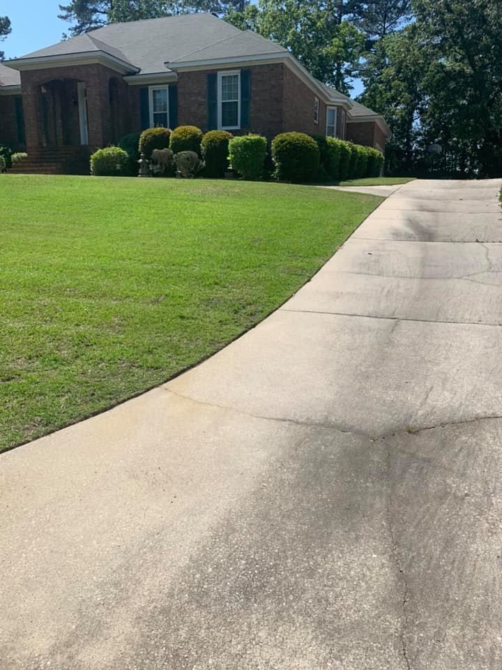 A brick house with a curved concrete driveway and green lawn.