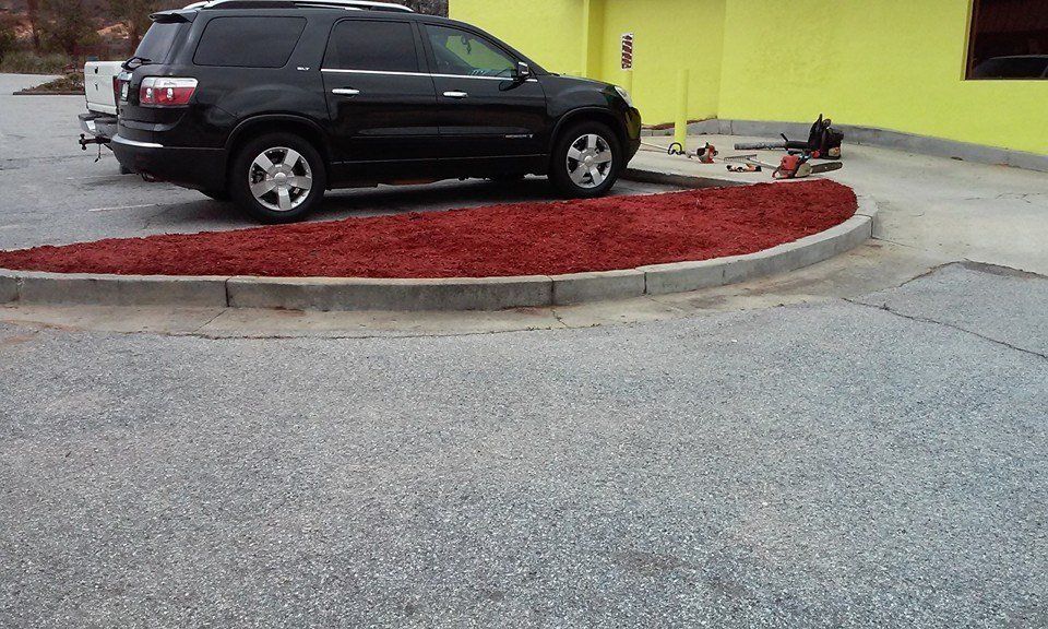 Black SUV parked next to a red mulch-filled landscape bed in front of a yellow building.