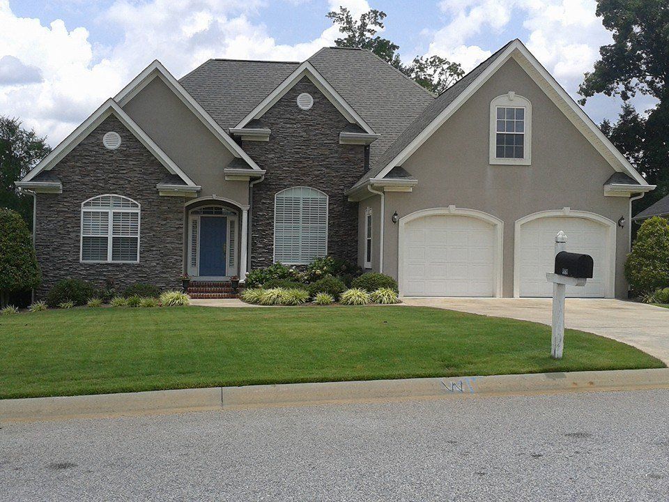 A two-story house with stone and stucco exterior, blue door, and two-car garage, on a green lawn.