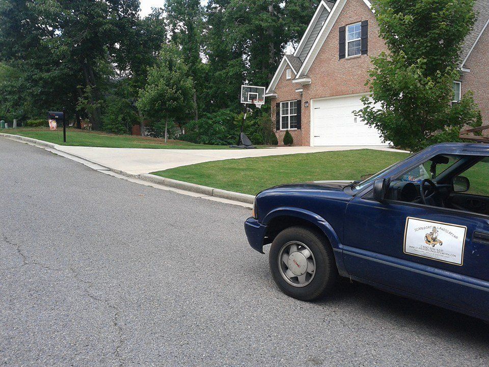 Blue truck parked on a street in front of a brick house with a basketball hoop in the driveway.