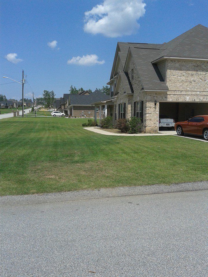 House with brick exterior, green lawn, blue sky, and cars in the garage on a sunny day.