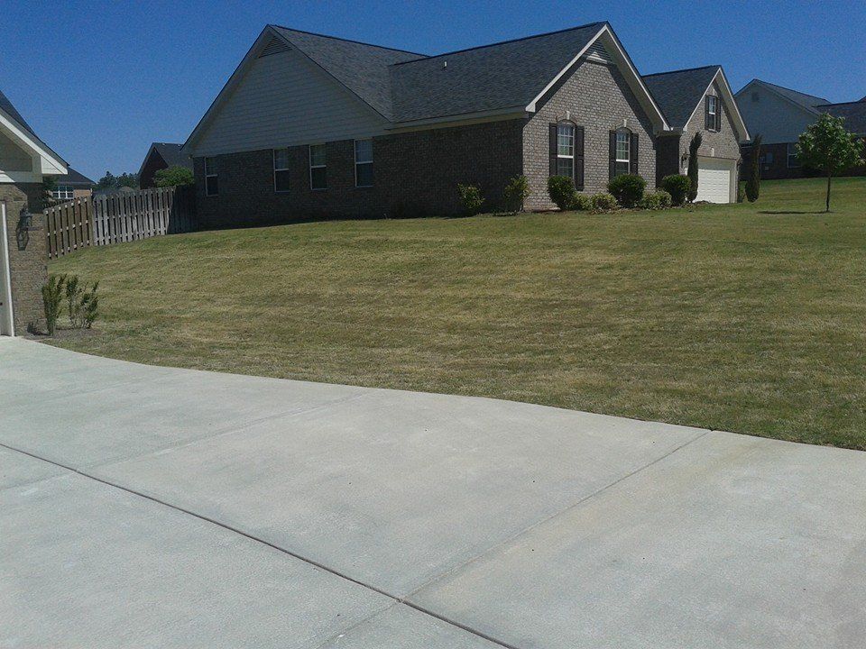 A single-story brick house with a dark roof and black shutters sits on a grassy hill on a sunny day.